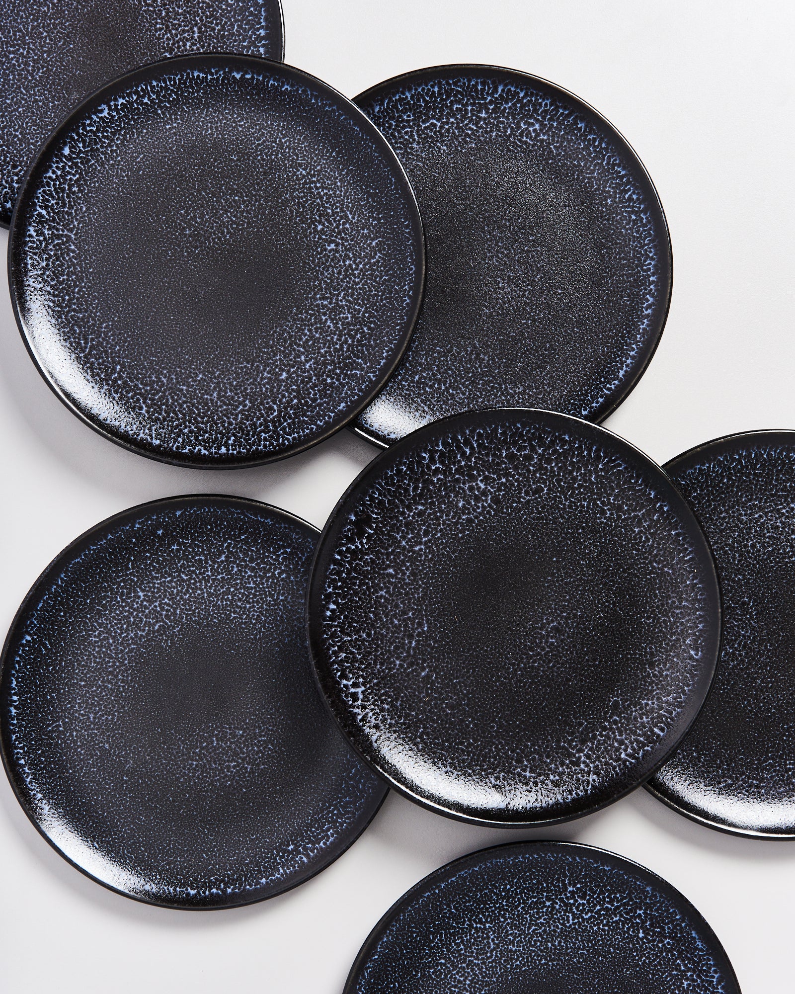 Schwarze Teller mit gesprenkeltem Muster, auf weißen Hintergrund angeordnet.