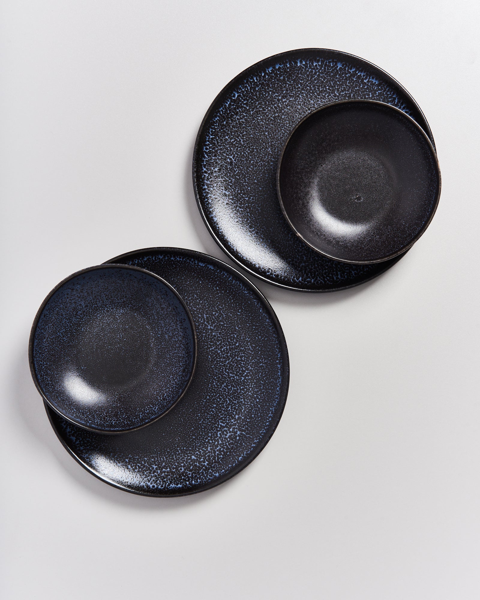 Zwei Sets aus blauen, gesprenkelten Tellern und Schüsseln auf einer hellen Oberfläche.