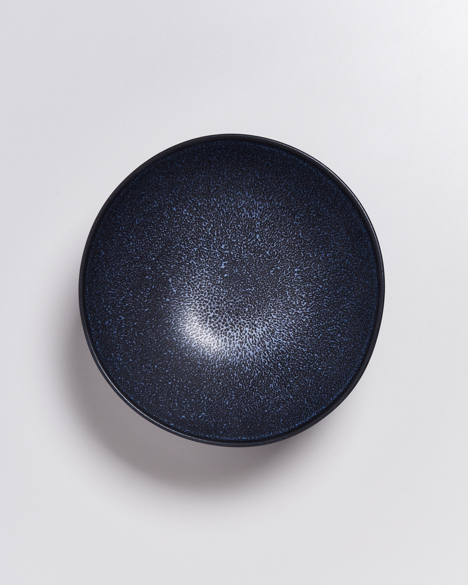 Dunkelblaue Schüssel mit gesprenkeltem Muster auf weißem Hintergrund.