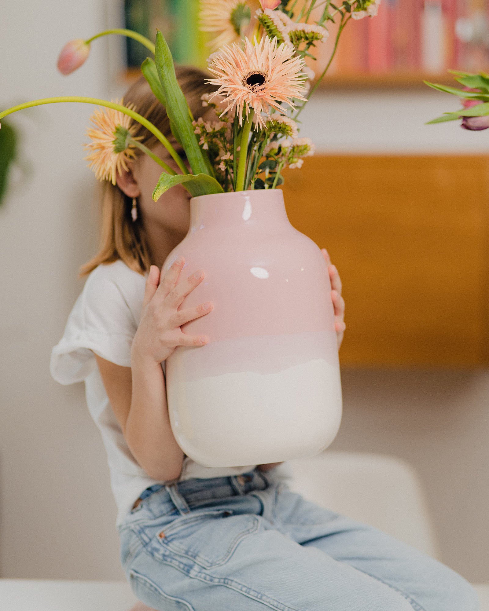 Ein Kind hält eine große, rosa-weiße Vase mit Pfirsichblumen, die das Gesicht verdecken.
