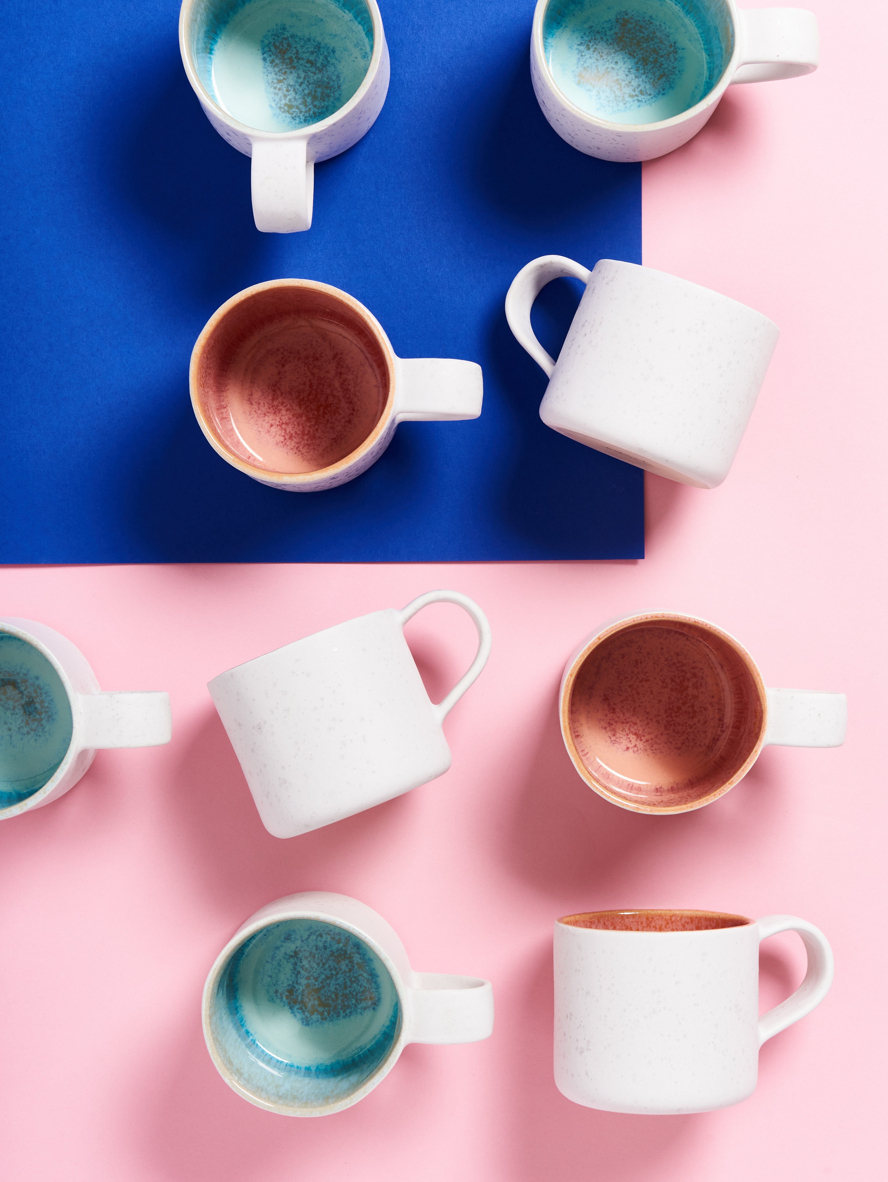 Verschiedene bunte Tassen auf einer blauen und rosa Oberfläche.