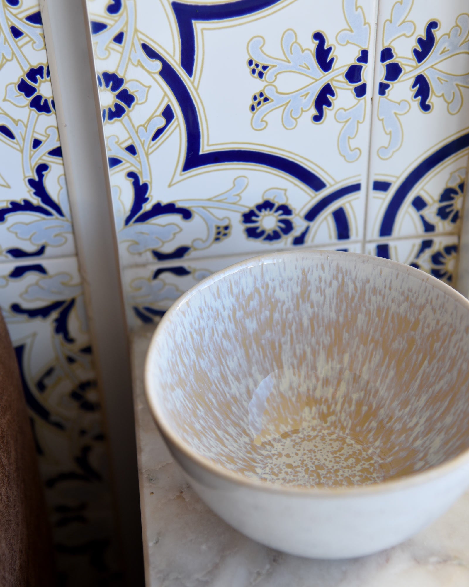 Keramikschale vor gemusterten blauen und weißen Fliesen auf einem Marmortisch.