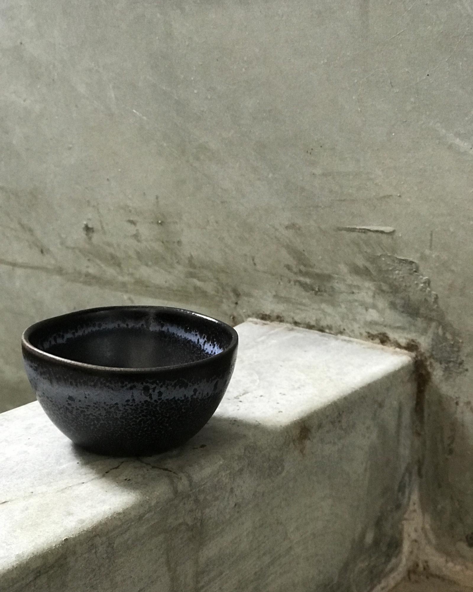 Schwarze Keramikschale auf einem grauen, abgenutzten Betonsims vor einer rauen Betonwand.