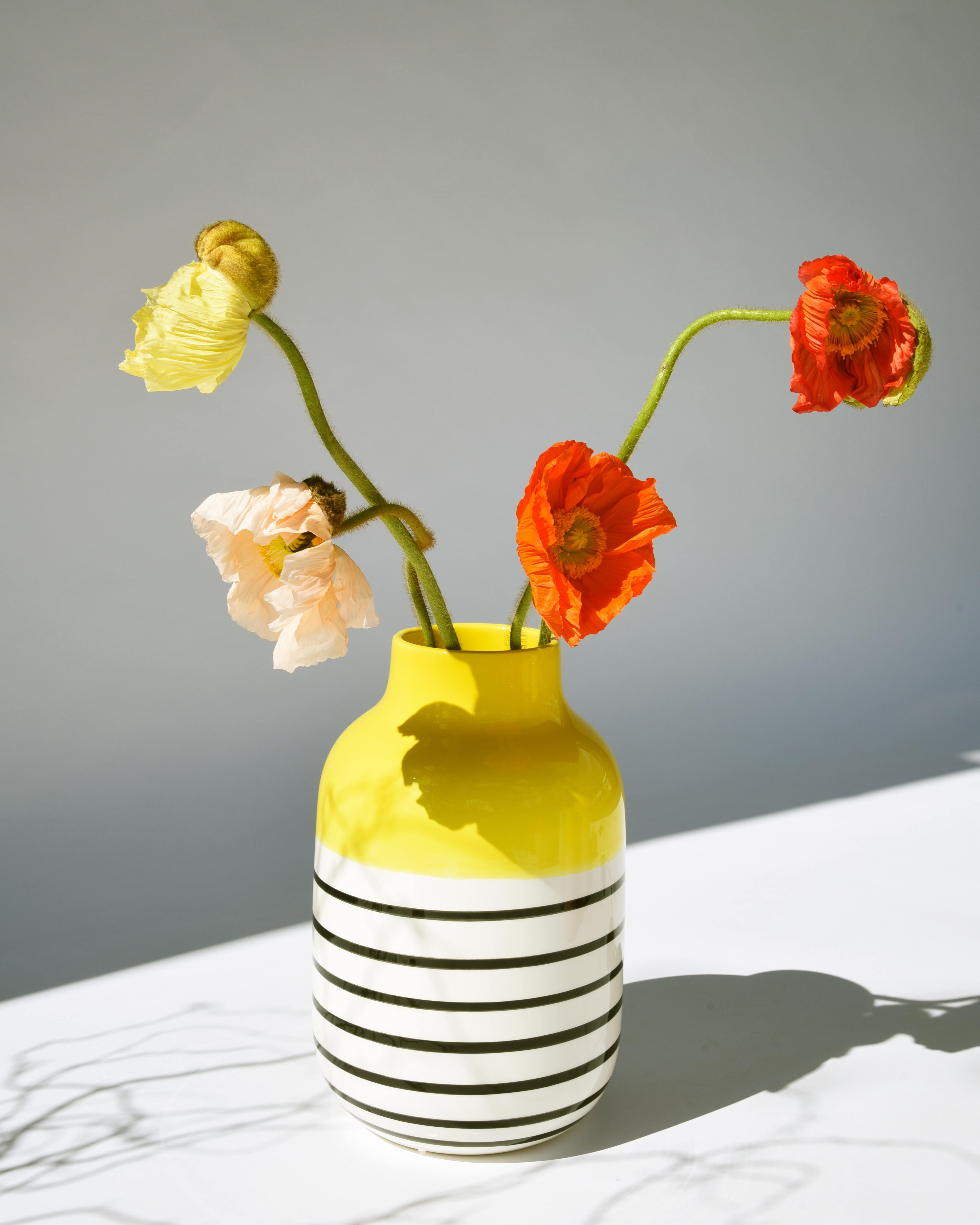 Gelber gestreifter Krug mit gelben und orangefarbenen Mohnblumen auf weißem Hintergrund.