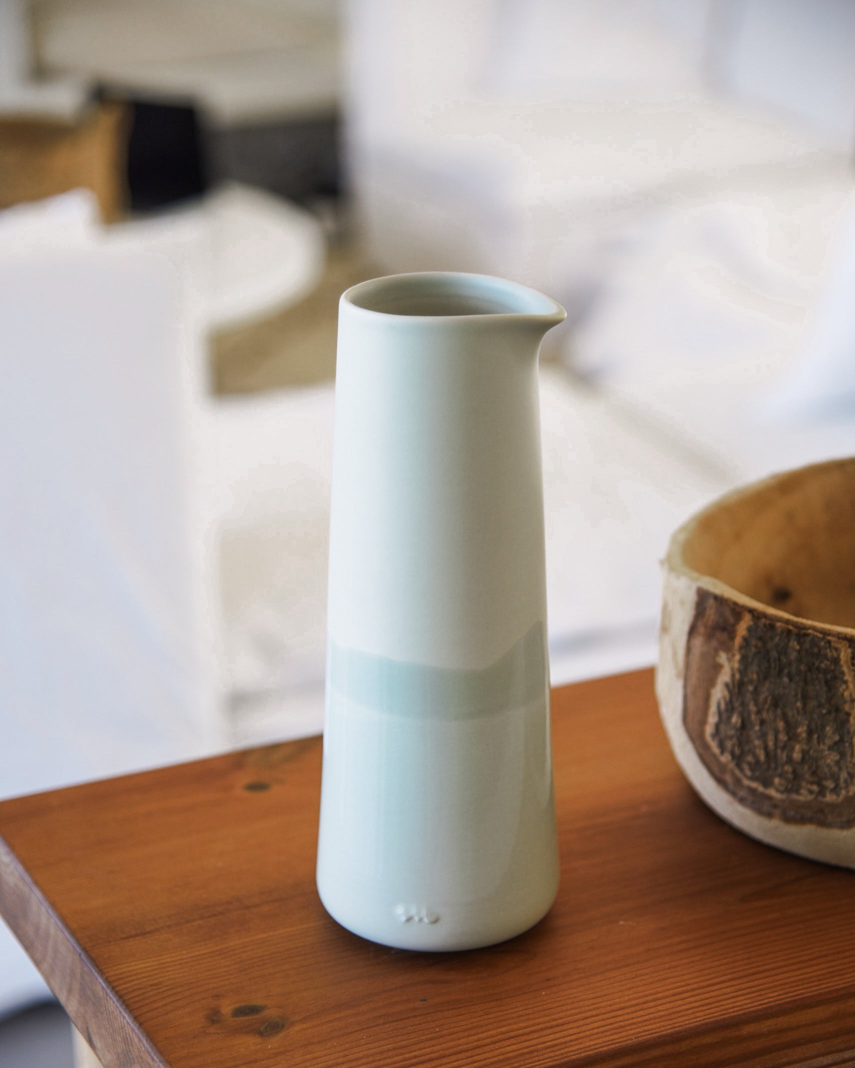 Keramikvase auf einem Holztisch, mit einem rustikalen Holzgefäß daneben.