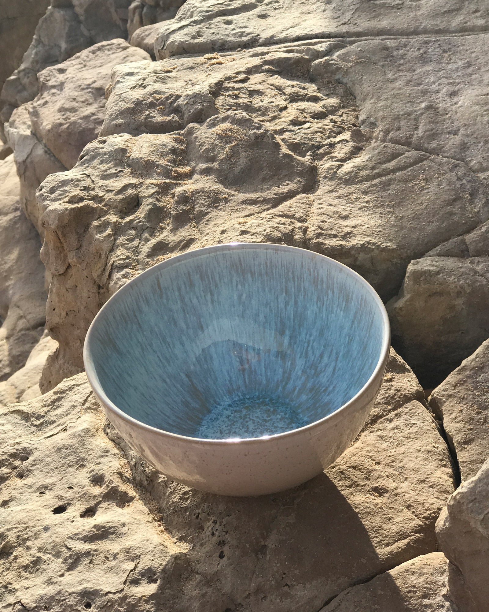 Keramikschüssel mit blauem Inneren steht auf einem felsigen Untergrund in der Sonne.
