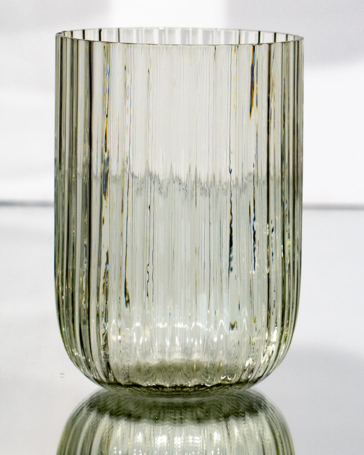 Klare, geriffelte Glasvase mit vertikalen Linien, auf glänzendem Untergrund stehend.