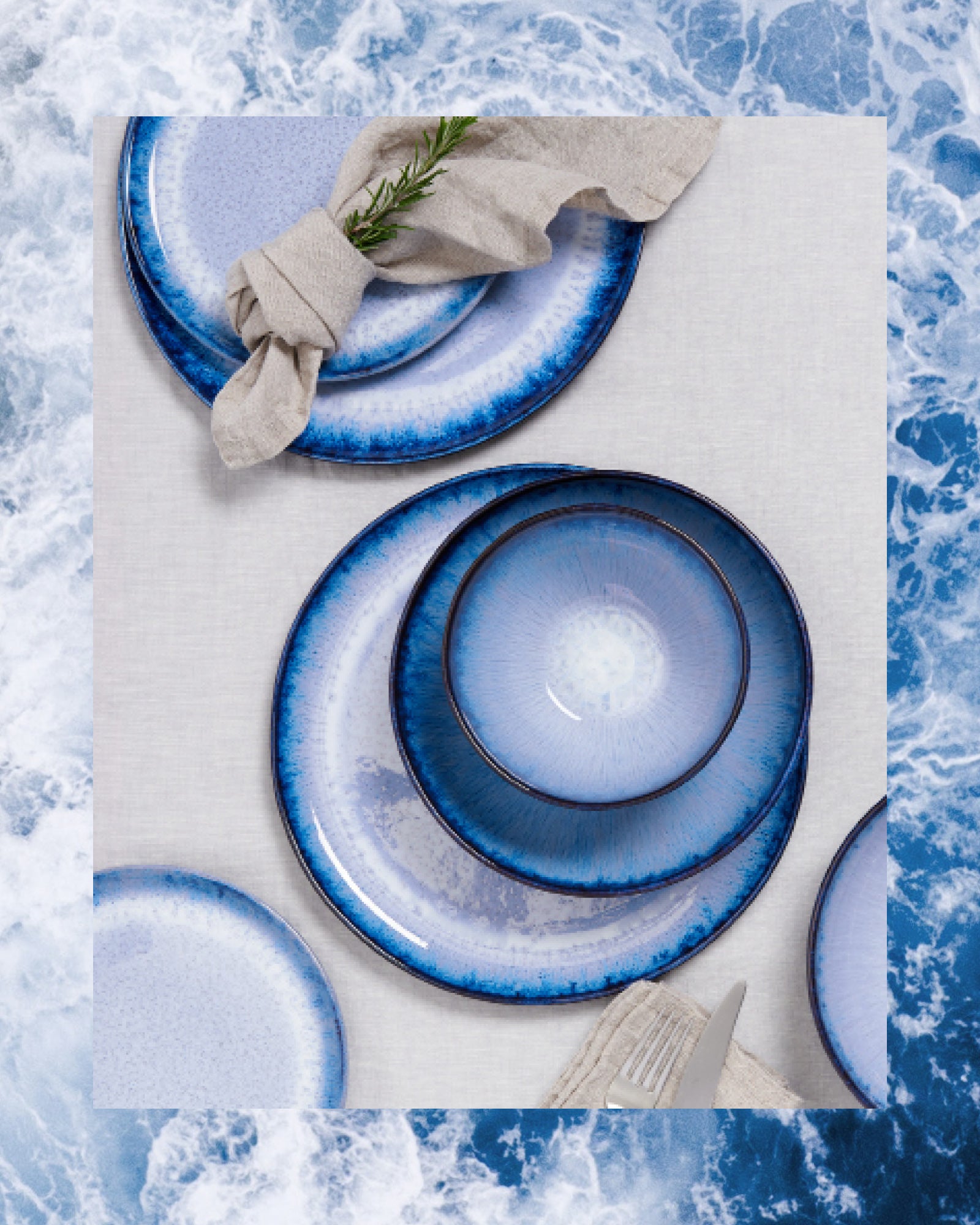 Blaue Teller mit dunklem Rand und gefaltete Serviette auf einem weißen Tuch, umgeben von Wasserhintergrund.