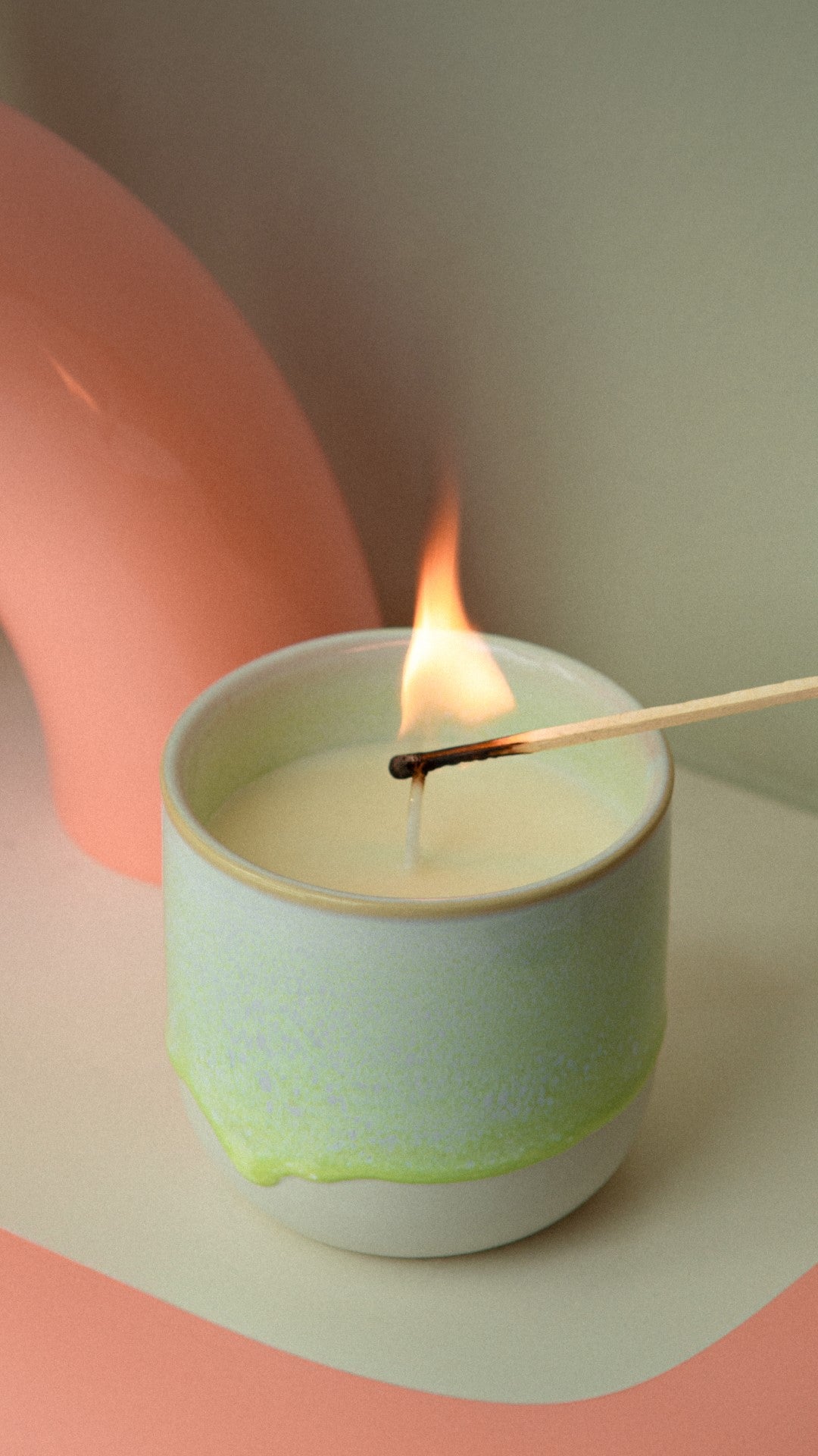 Ein brennendes Streichholz entzündet eine Kerze in einem pastellfarbenen Raum.