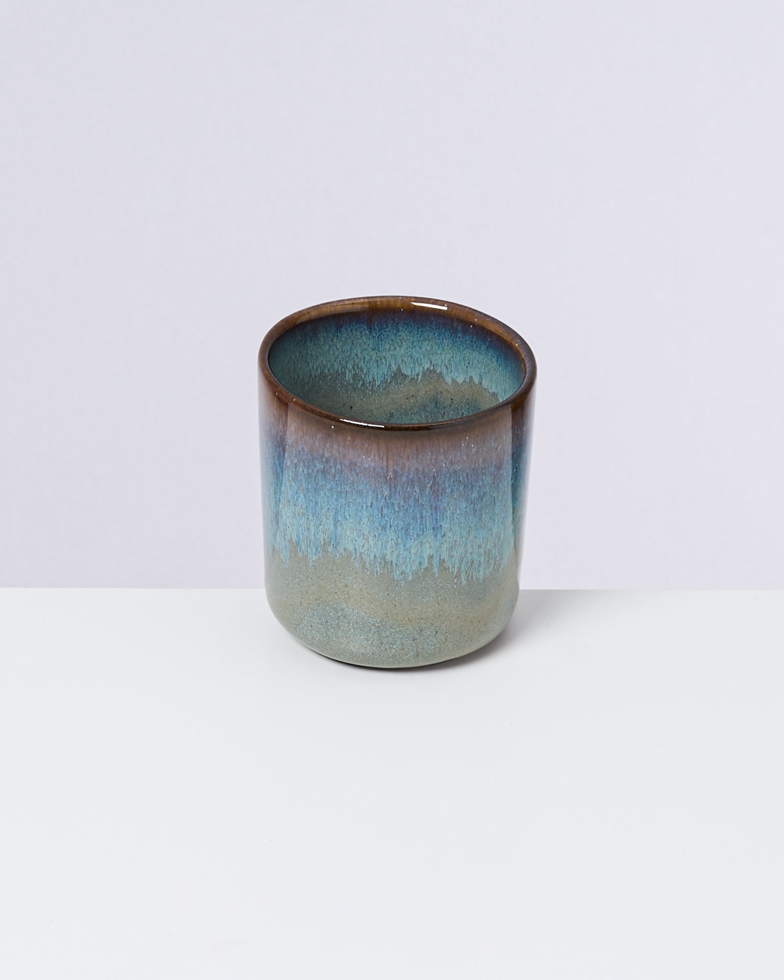 Keramikbecher mit braun-blauer Glasur auf weißem Hintergrund.