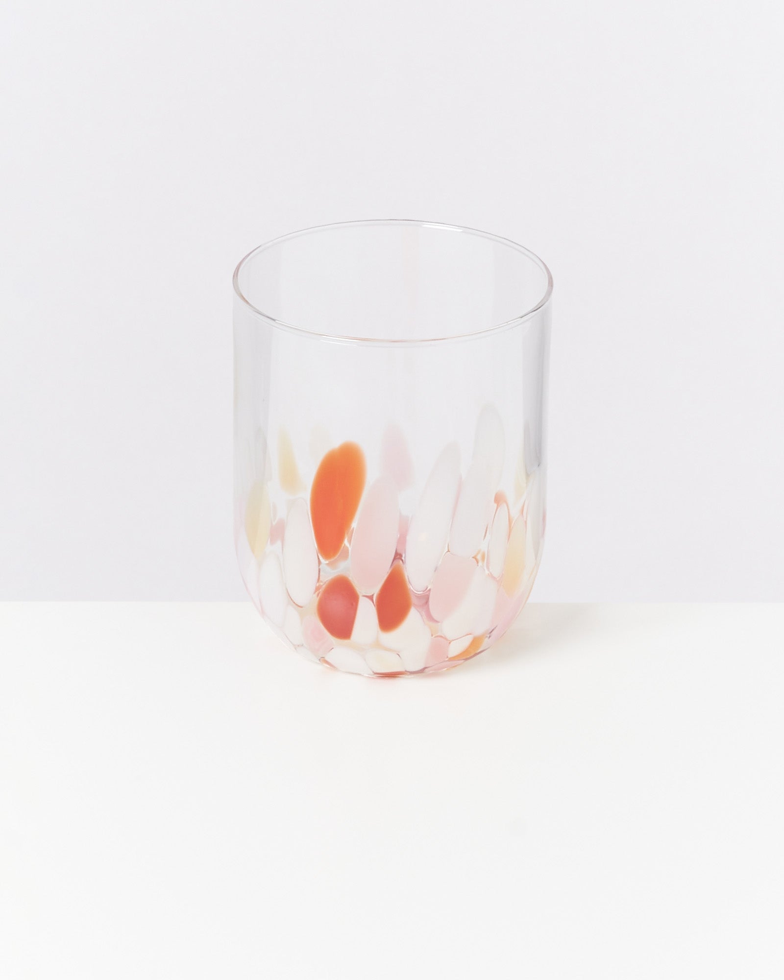 Ein Glas mit orangefarbenen und weißen Punkten steht auf einer weißen Oberfläche.