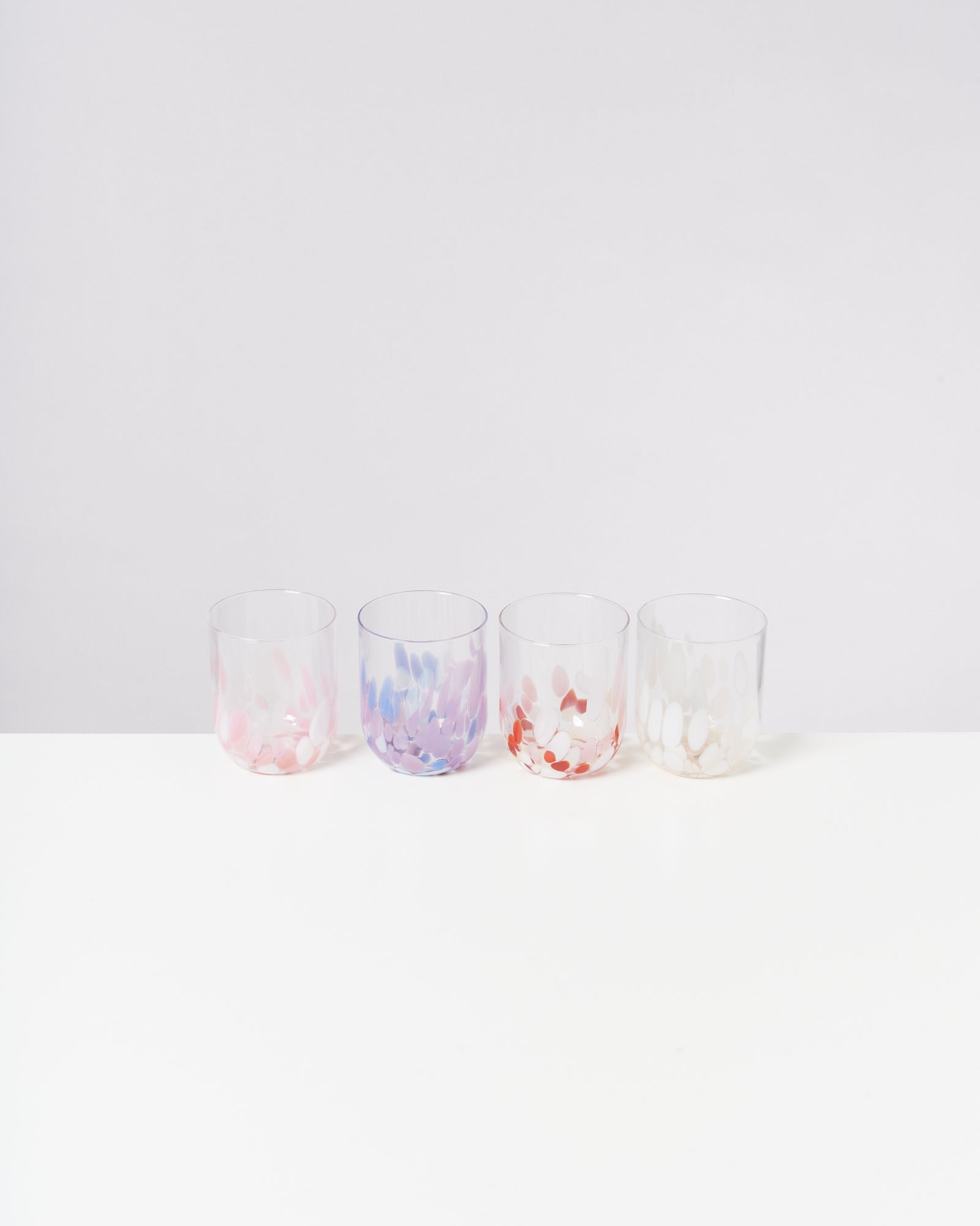 Vier bunte Trinkgläser mit dekorativen Mustern stehen in einer Reihe auf einem weißen Hintergrund.