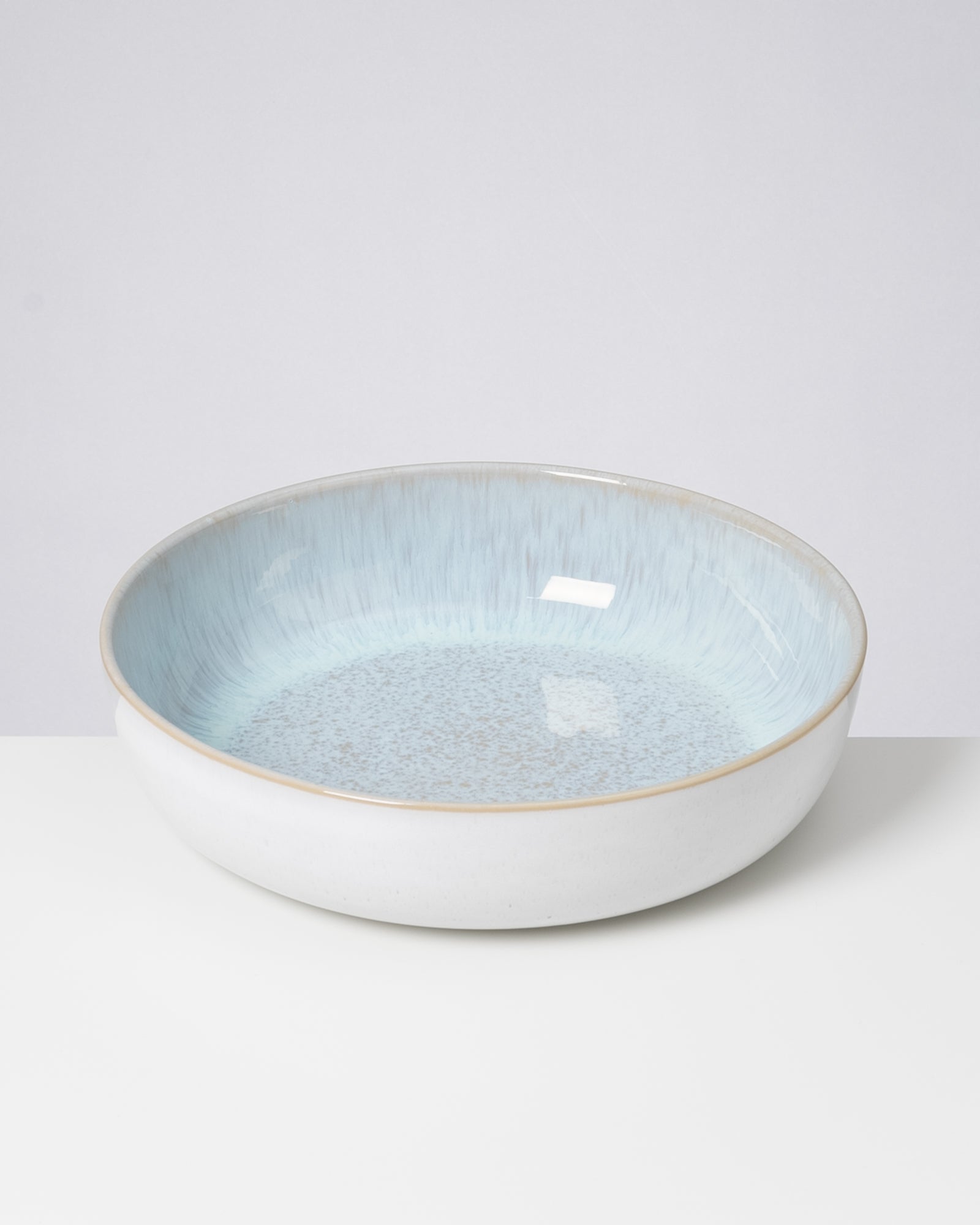 Eine flache, runde Schüssel mit blauer Innenseite und weißem Rand vor grauem Hintergrund.