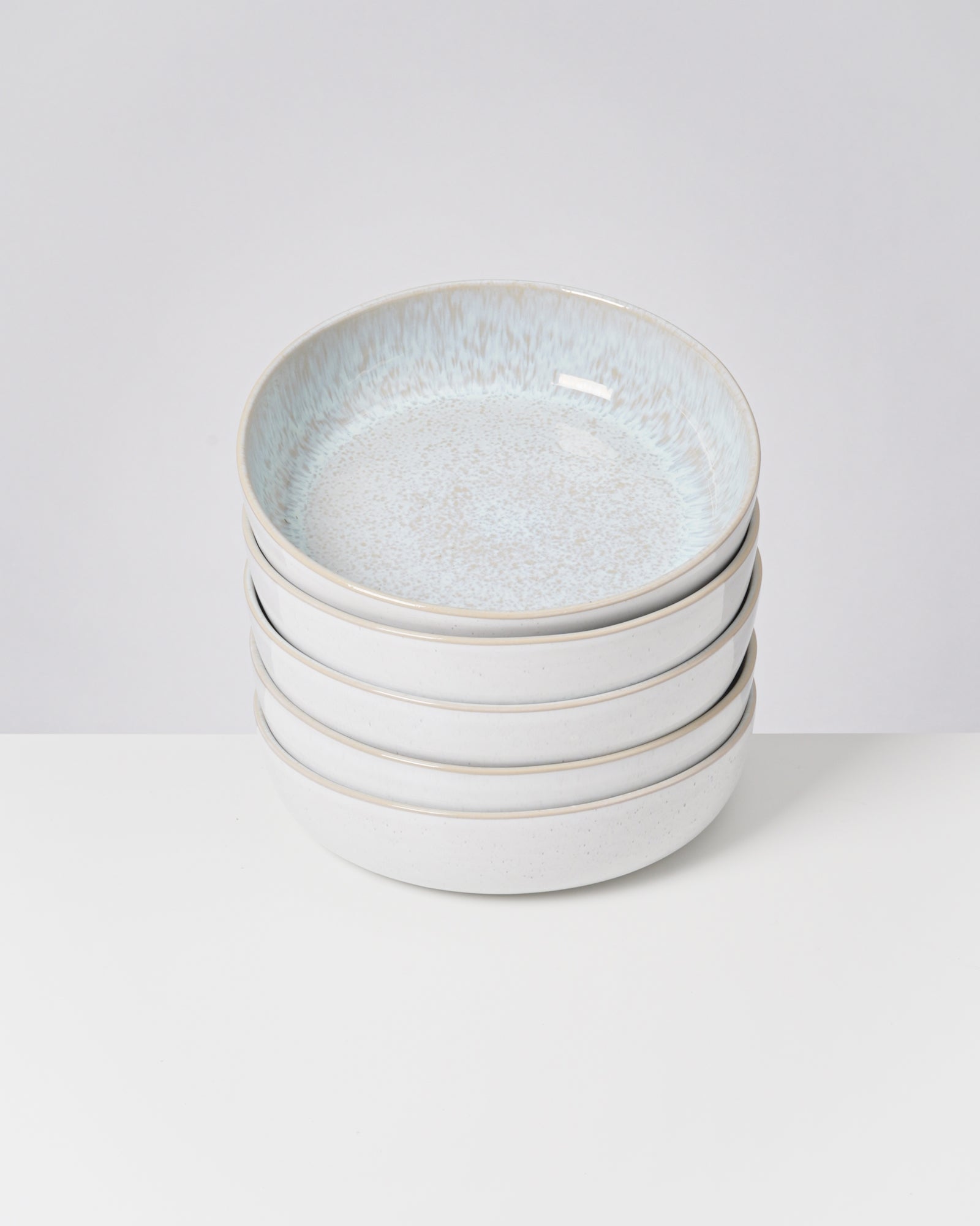 Vier gestapelte, helle Keramikteller mit leichtem blauen Muster auf weißem Hintergrund.