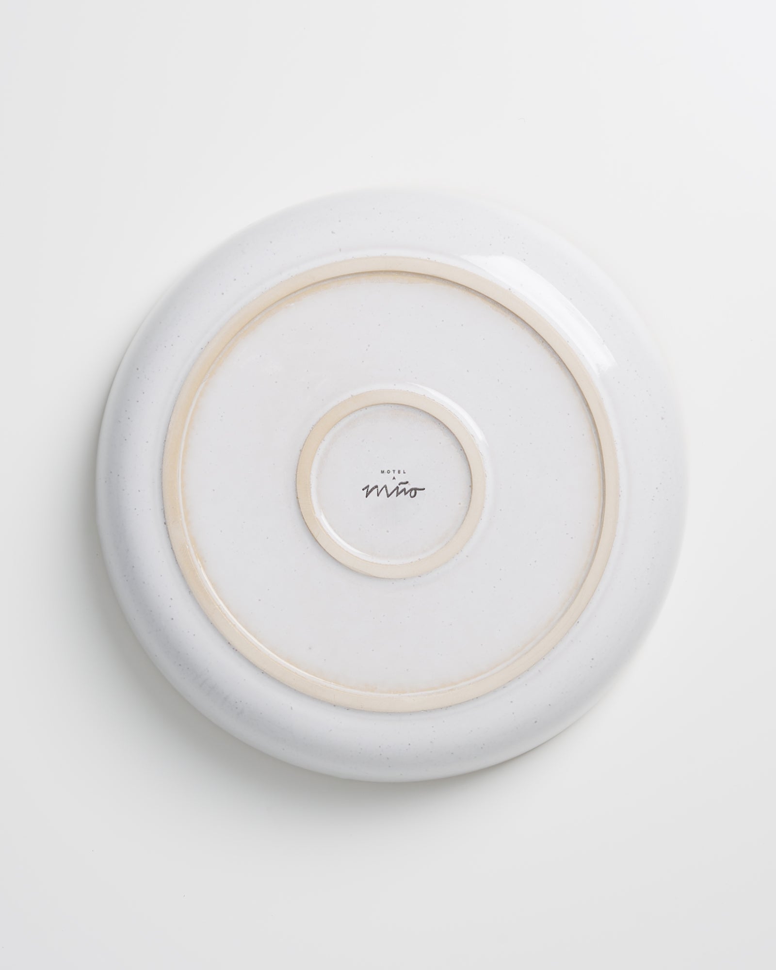 Weiße, umgedrehte Keramikplatte mit zwei konzentrischen, beigen Kreisen und einem Logo in der Mitte auf weißem Hintergrund.