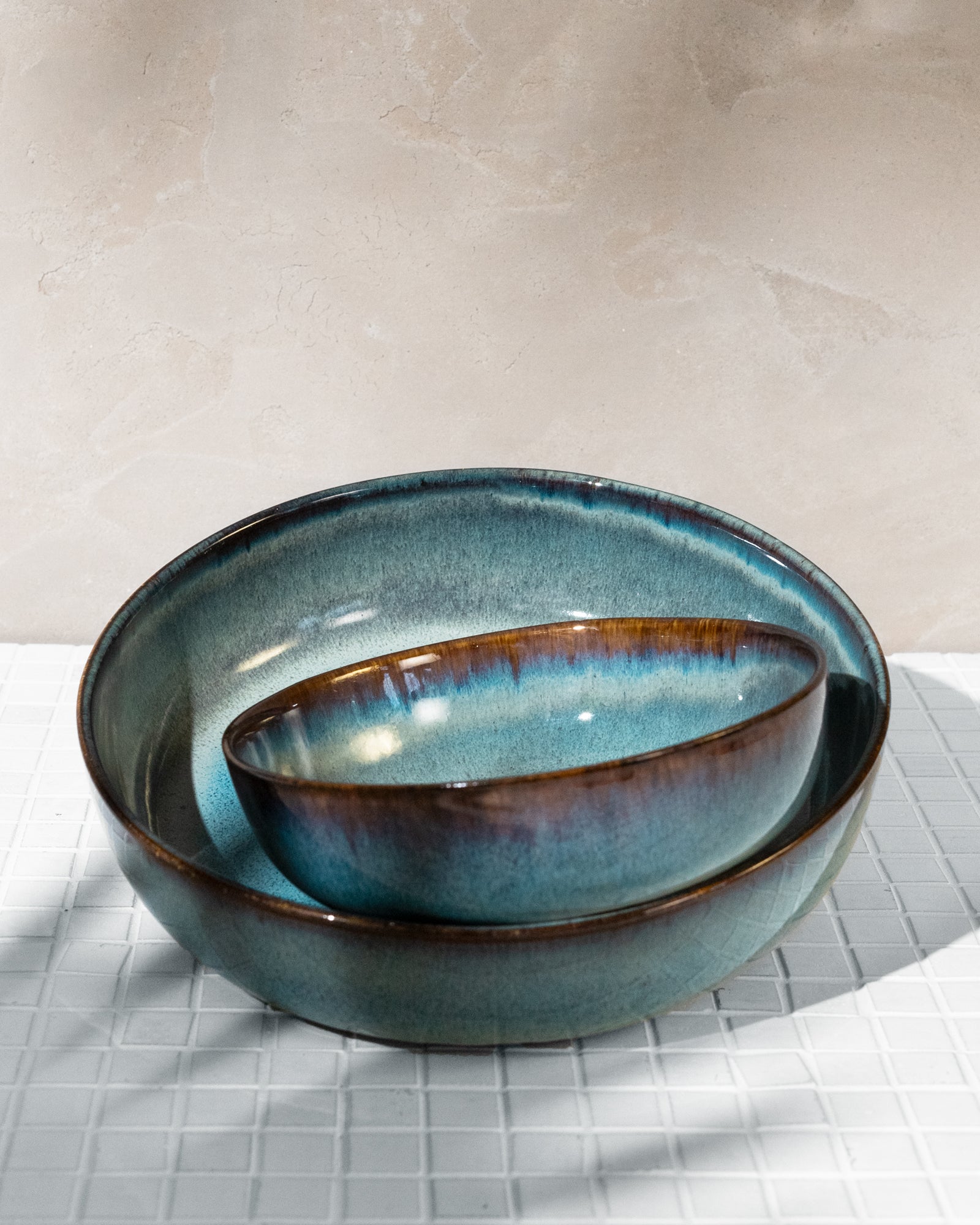 Zwei ineinander gestapelte, blau und braun glasierte Schalen auf einem weißen Fliesentisch.