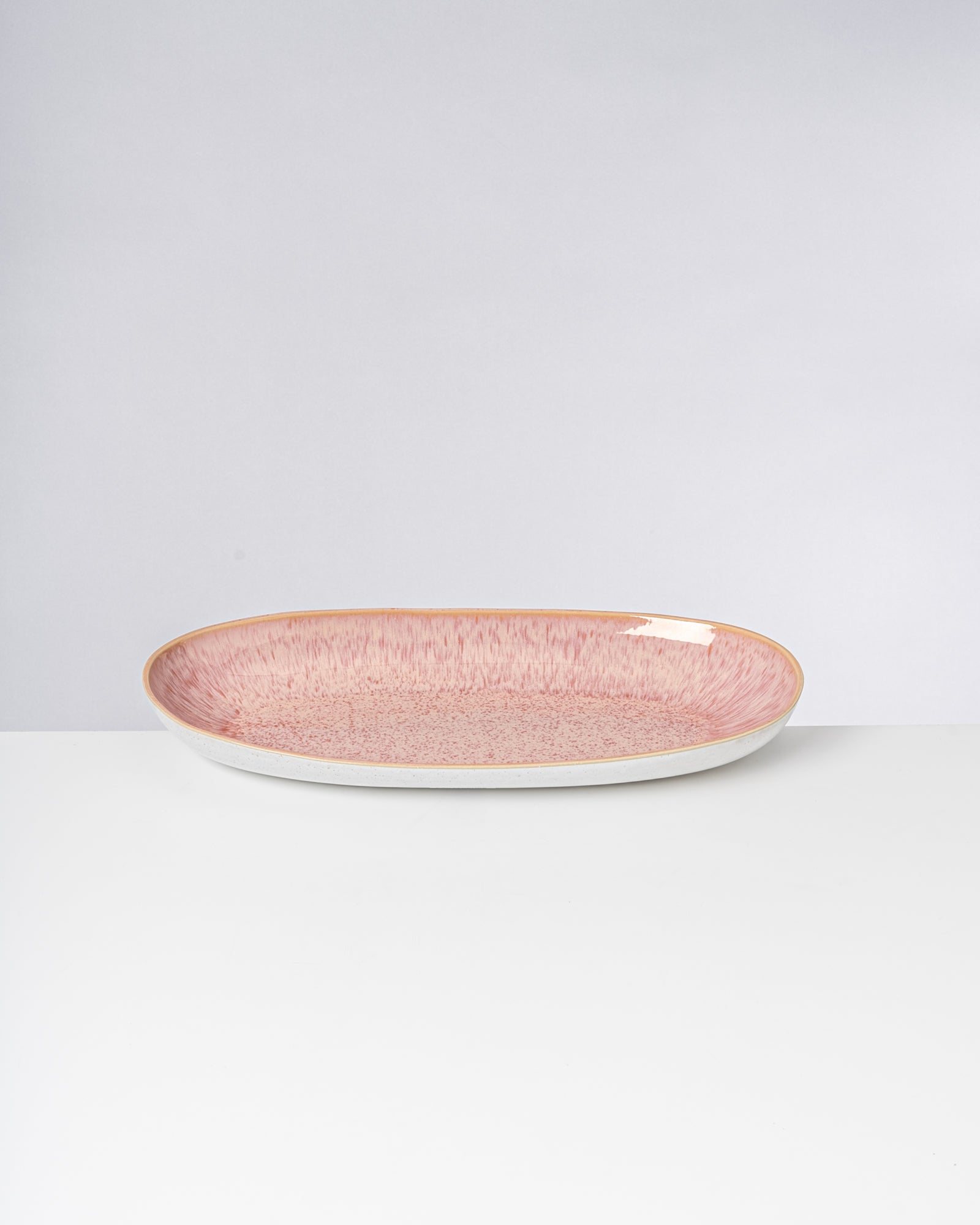 Ovale, rosa und beige Keramikschale mit einem abstrakten Muster auf einem weißen Hintergrund.