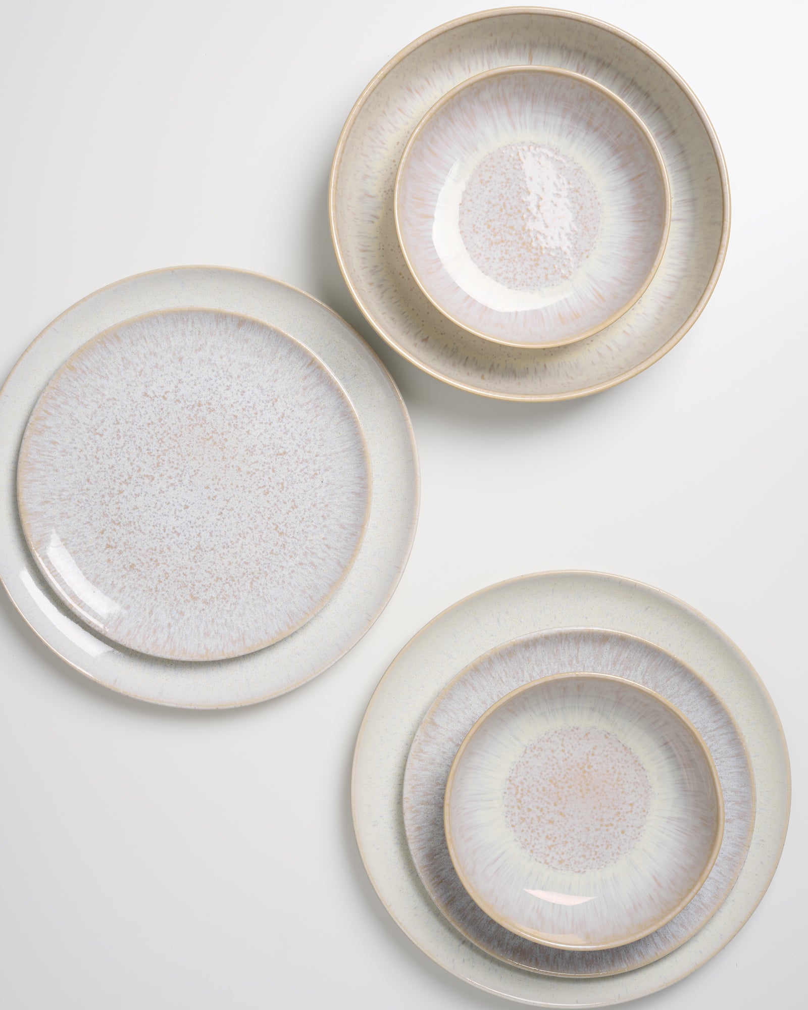 Drei Sätze von hellen, marmorierten Tellern und Schüsseln auf einem weißen Hintergrund.