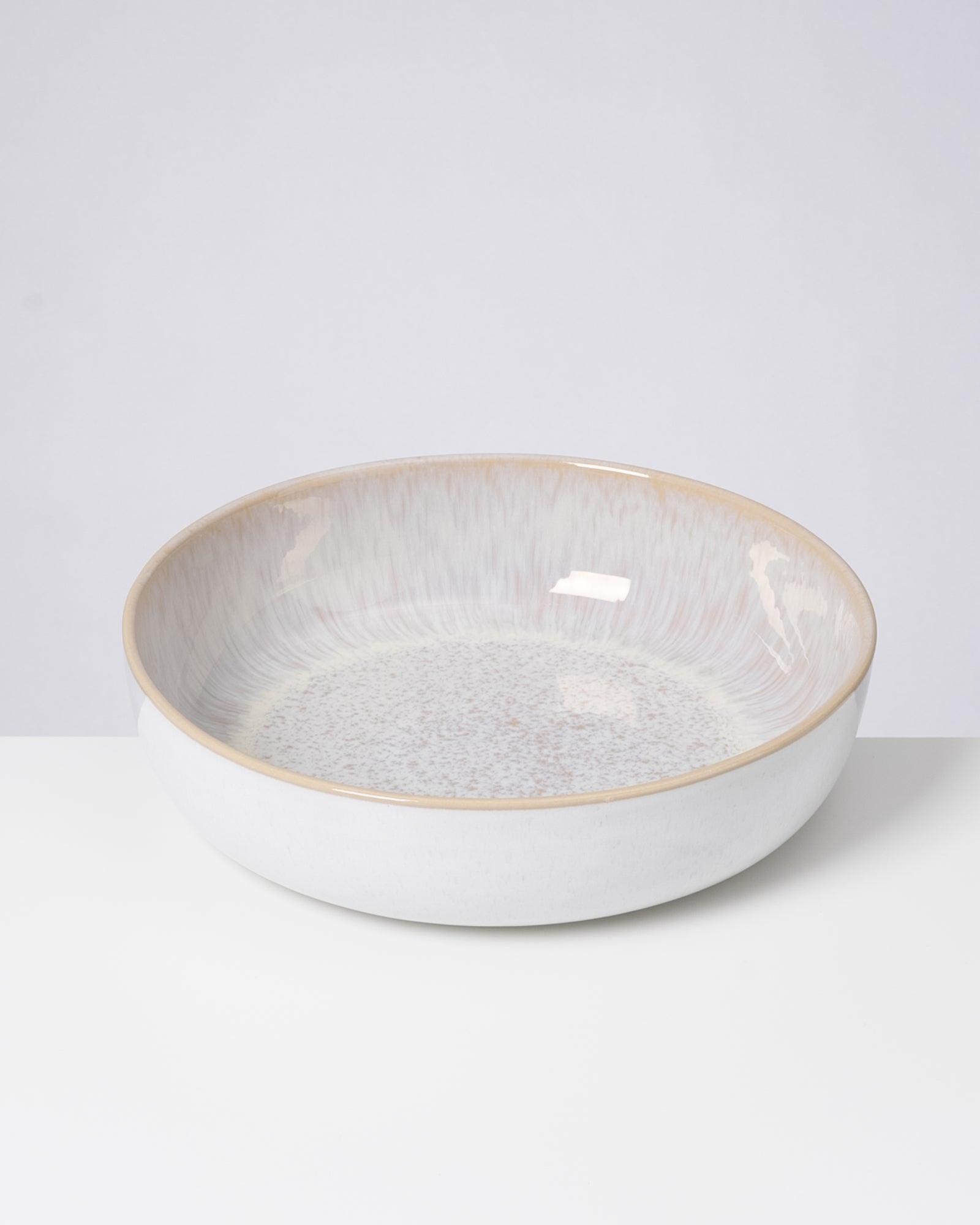 Keramikschüssel mit cremefarbenem Rand und gesprenkeltem Muster steht auf einem weißen Hintergrund.