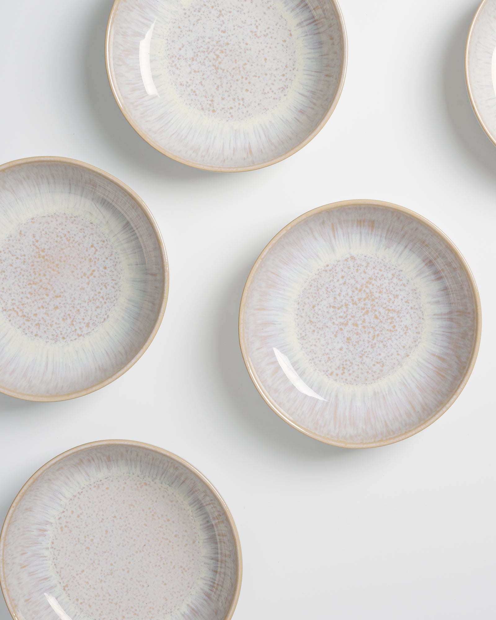 Fünf beige Teller mit gesprenkeltem Muster und weißem Rand auf weißem Hintergrund.