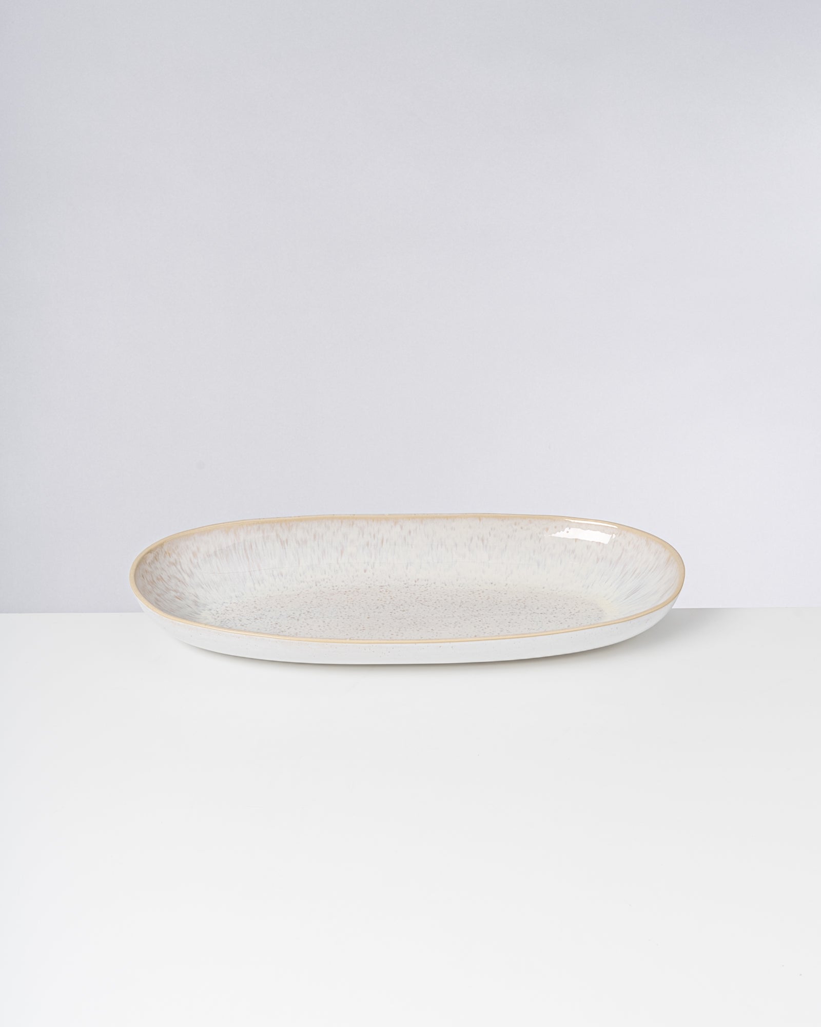 Ovaler, weißer Keramikteller mit leichtem Farbverlauf und minimalistischem Design auf weißem Hintergrund.