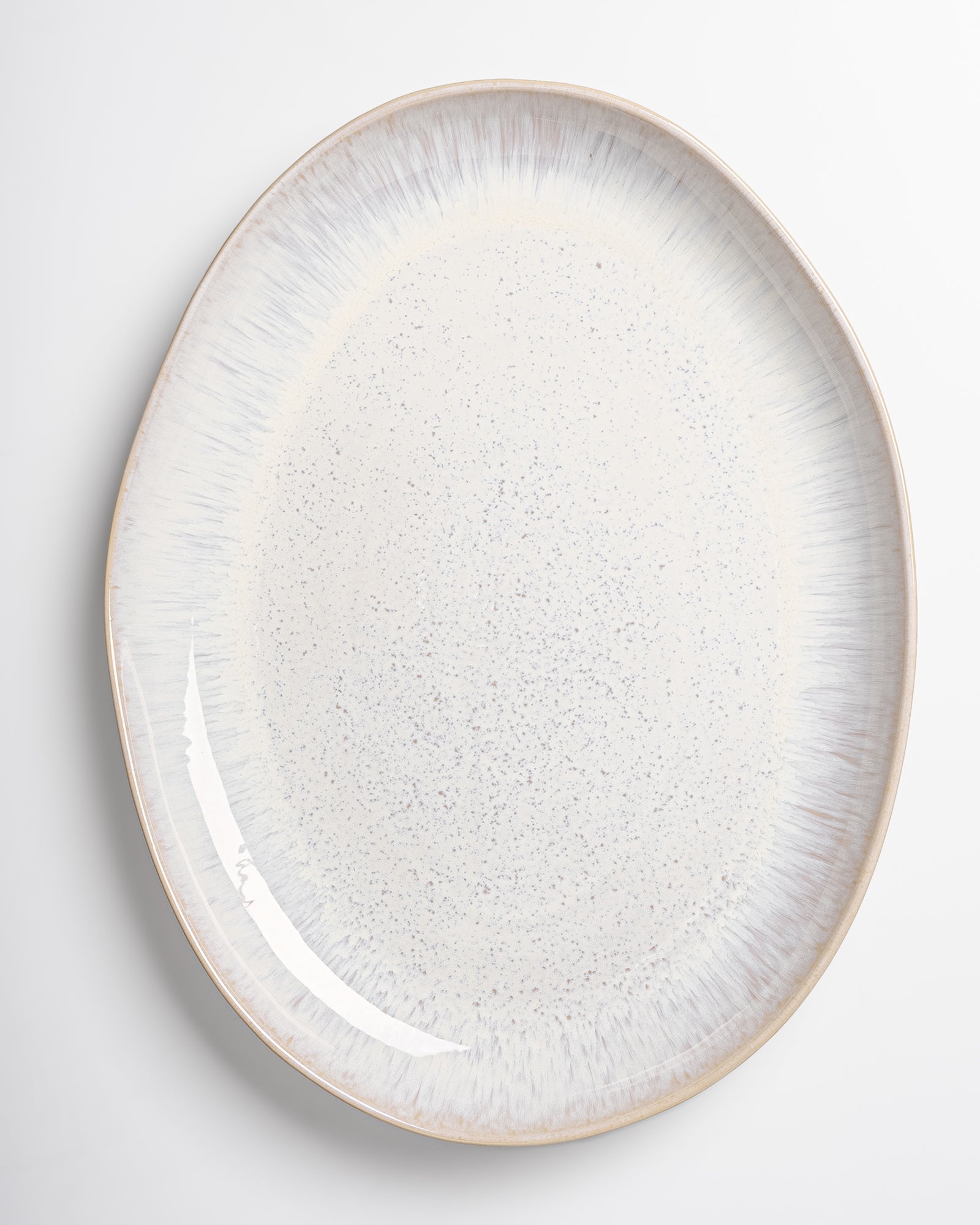 Asymmetrischer, ovaler Keramikteller mit weißem und gesprenkeltem Muster auf einem weißen Hintergrund.
