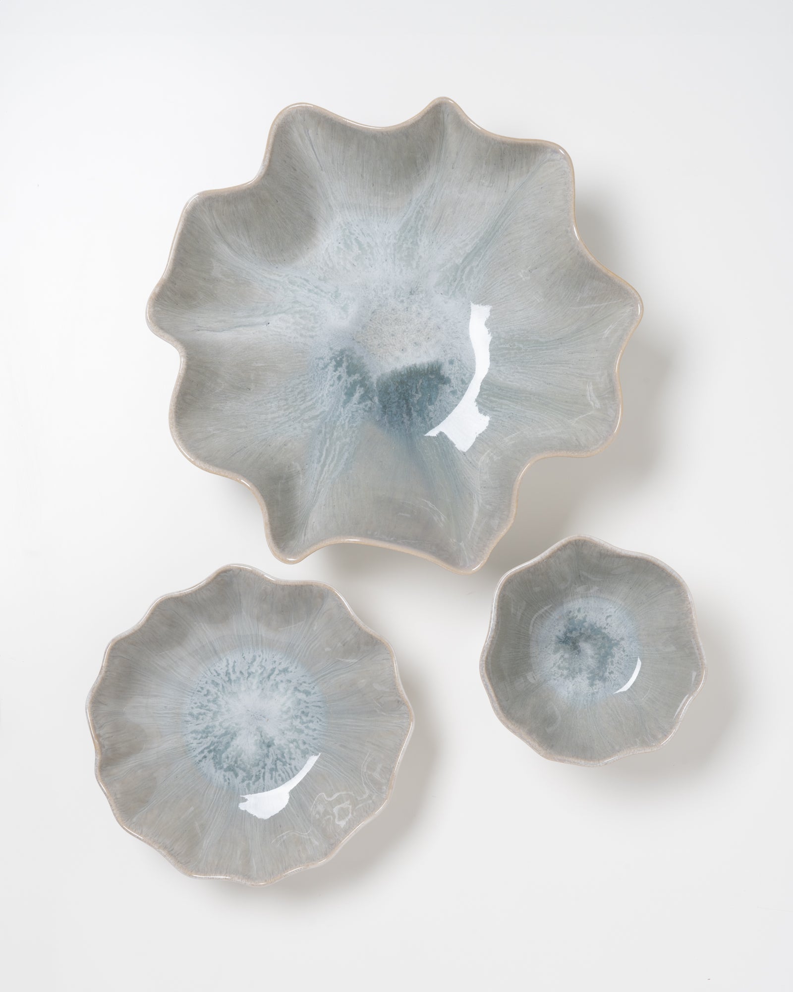 Drei graublaue, blumenförmige Keramikschalen in verschiedenen Größen auf weißem Hintergrund.