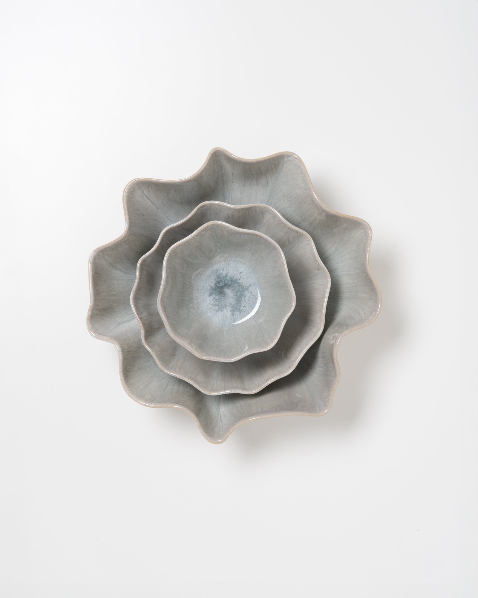 Drei graue, blumenförmige Keramikteller ineinander gestapelt auf weißem Hintergrund.