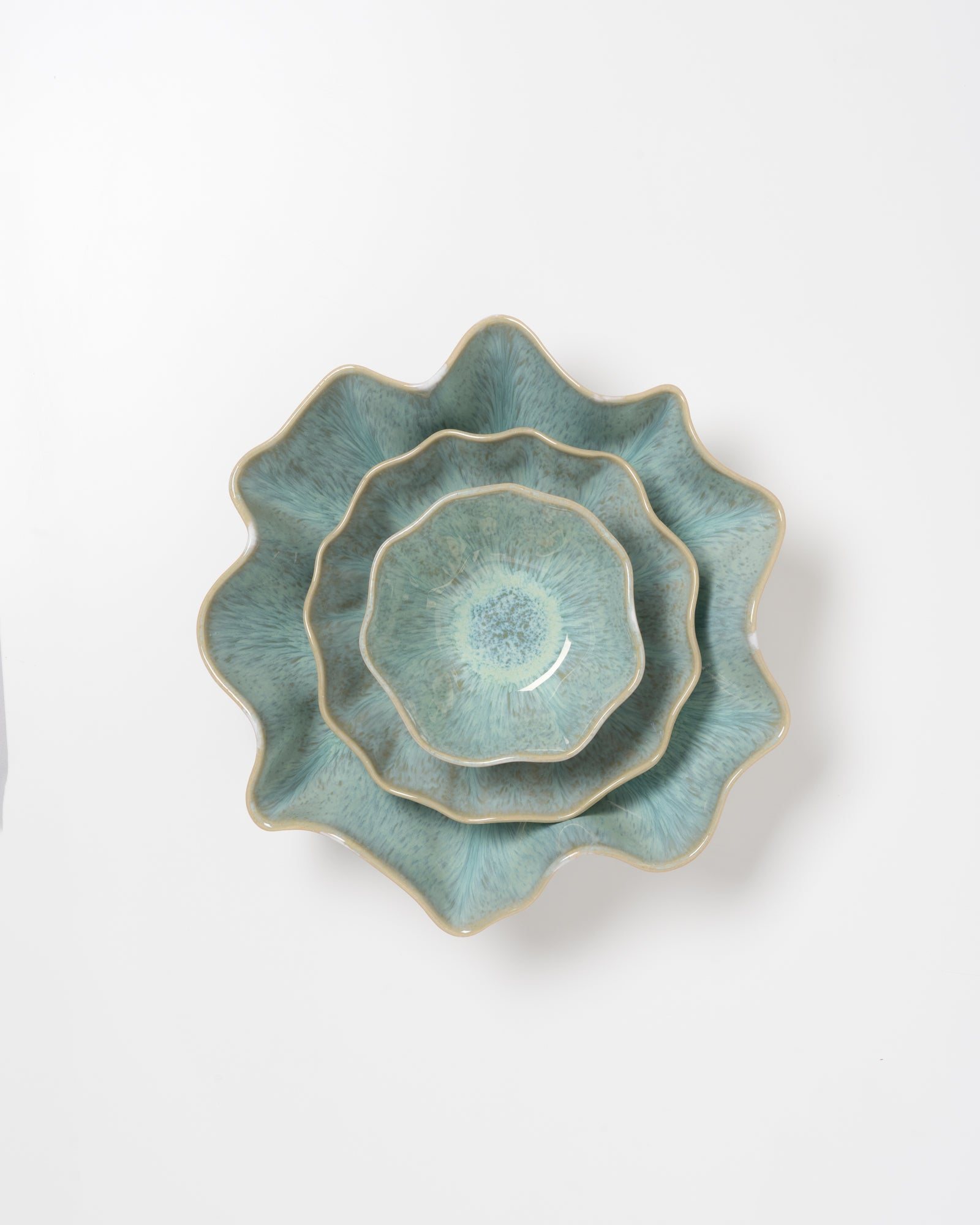 Drei übereinander gestapelte, grüne, wellenförmige Keramikschalen auf weißem Hintergrund.