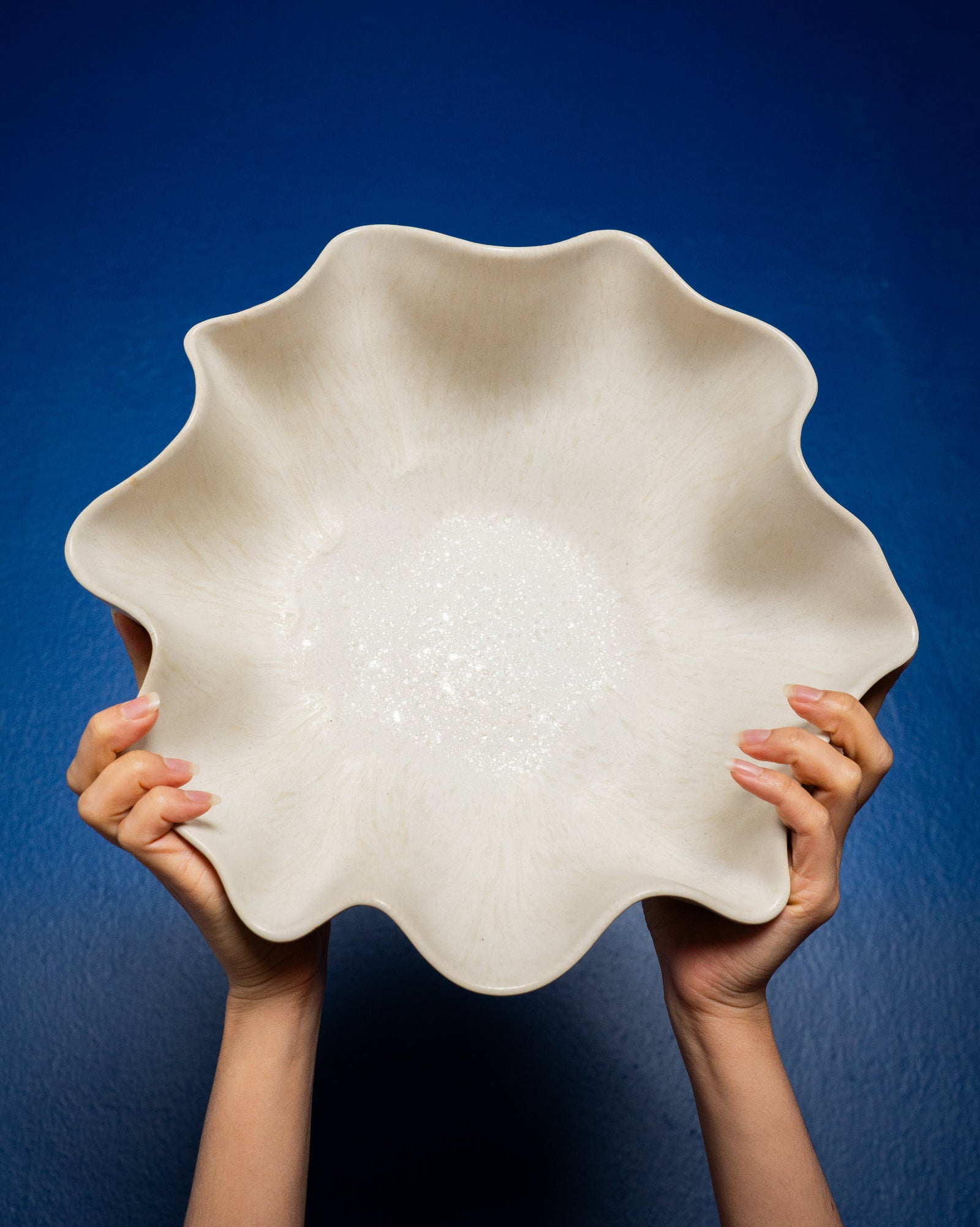 Zwei Hände halten eine gewellte, weiße Schüssel gegen einen kobaltblauen Hintergrund.