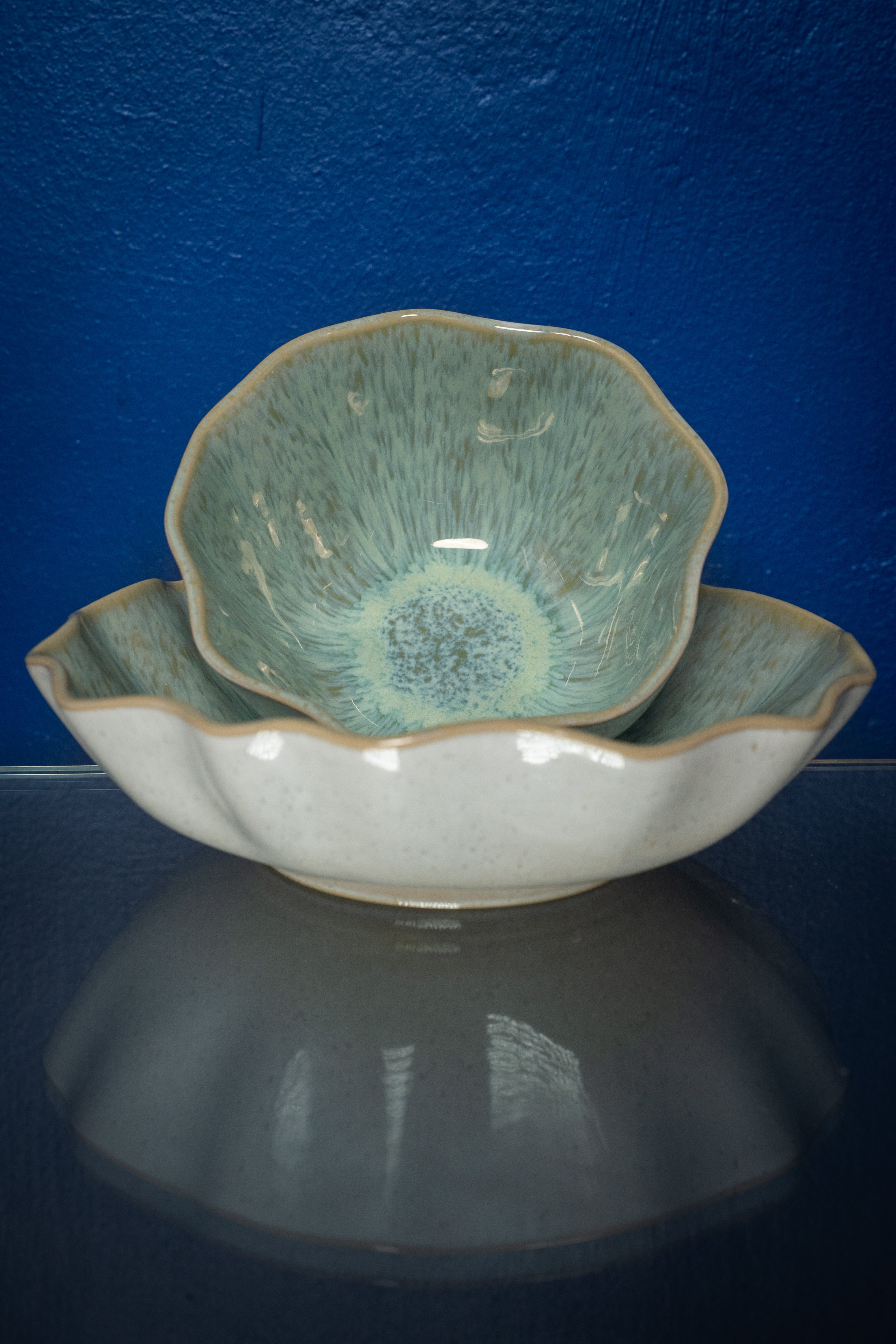 Zwei ineinander gestapelte, blumenförmige Schalen mit grünlicher Glasur vor blauem Hintergrund.