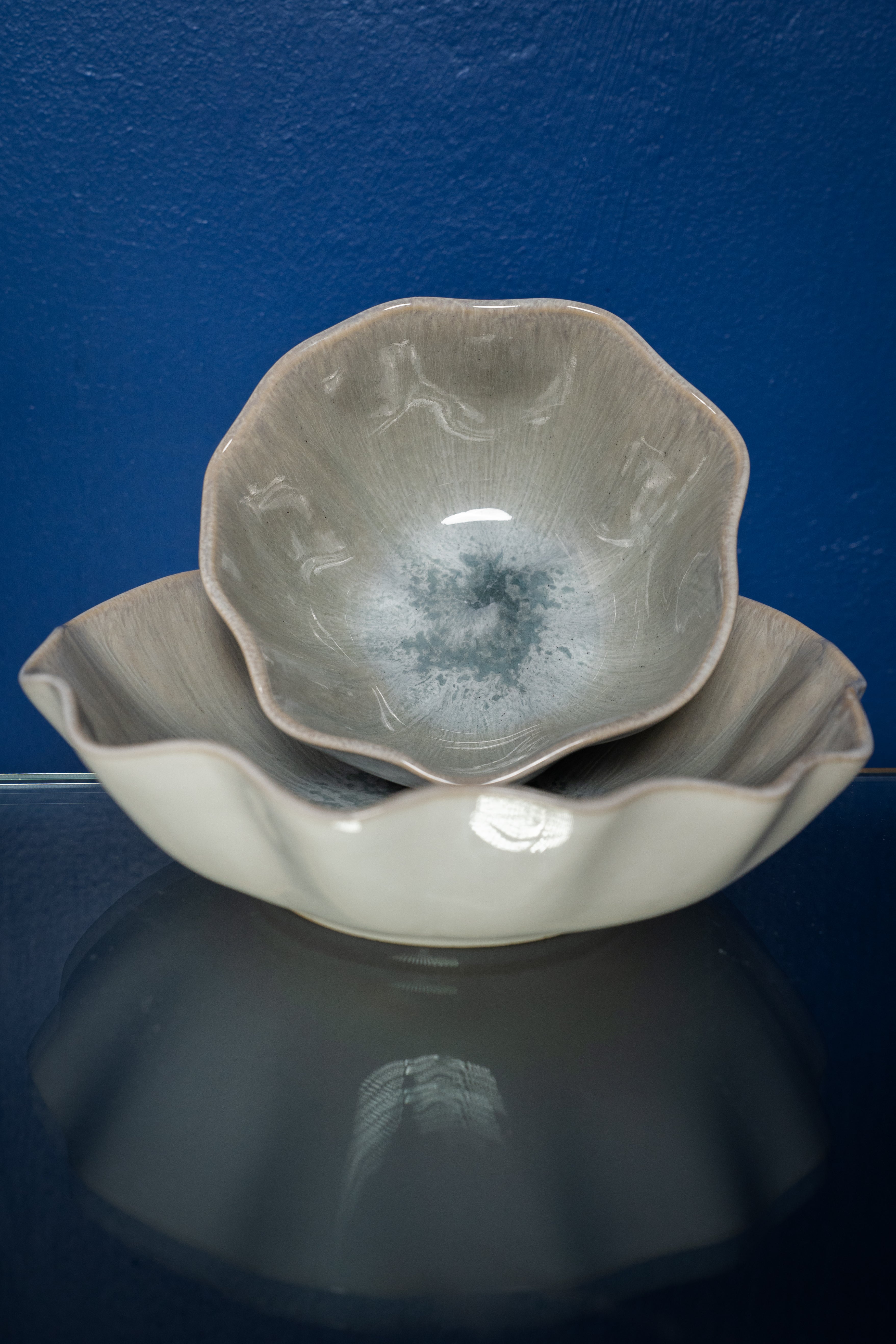 Zwei Schüsseln mit welligem Rand in Grautönen, ineinander gestapelt vor einem blauen Hintergrund.