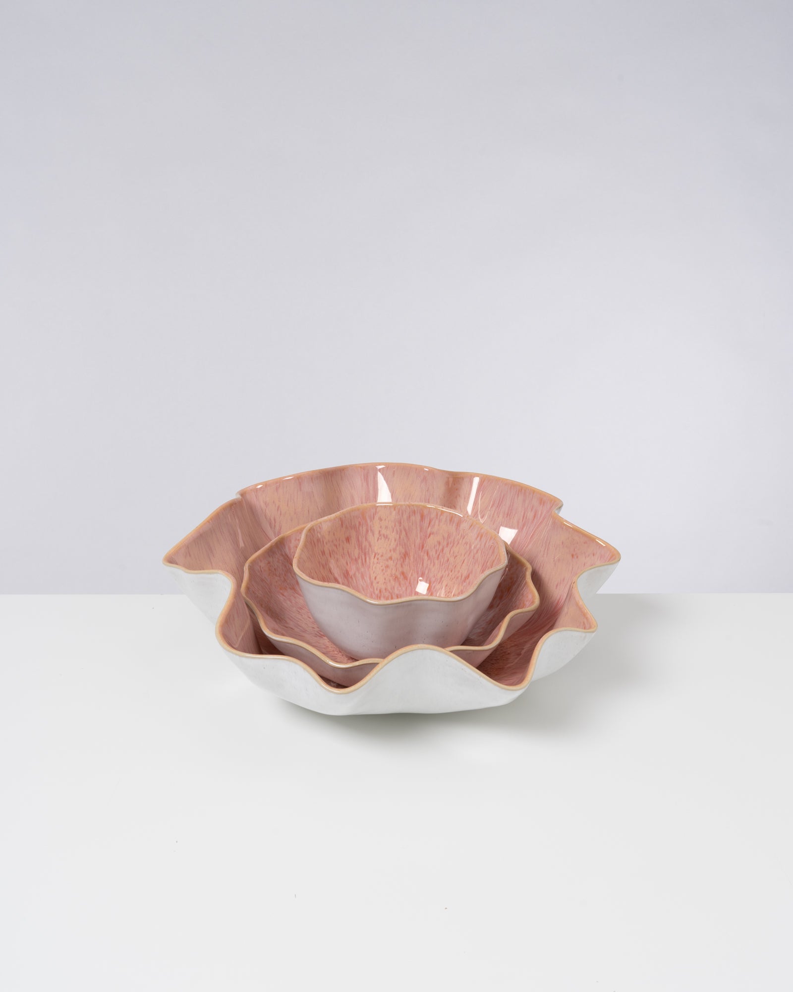Drei ineinander gestapelte, wellenförmige Schalen in Rosa und Weiß auf weißem Hintergrund.