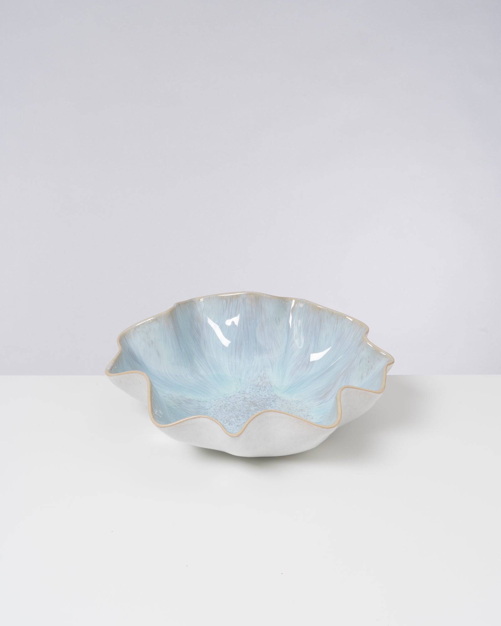Keramikschale mit gewelltem Rand und glänzender, hellblauer Glasur auf weißem Hintergrund.