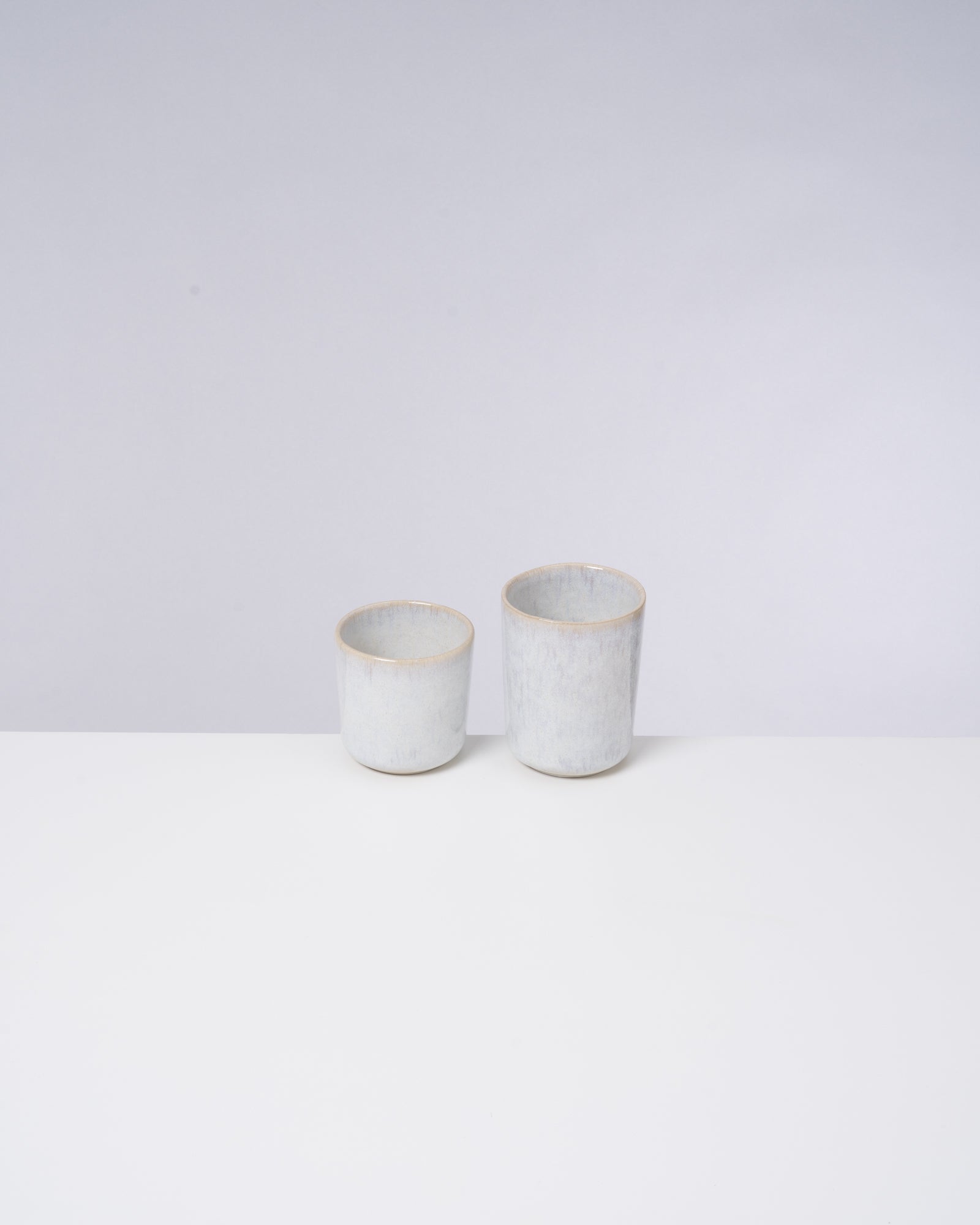 Zwei weiße, zylindrische Keramiktassen in unterschiedlicher Größe stehen auf einem weißen Hintergrund.