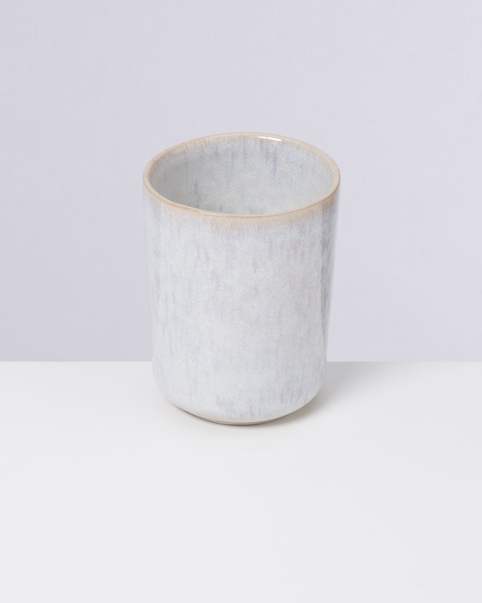 Ein einfacher, heller Keramikbecher vor einem grauen Hintergrund.