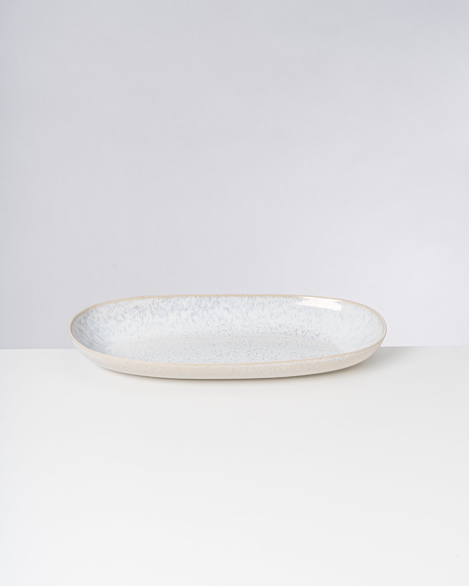 Ein ovaler, flacher, cremefarbener Teller mit blauer, gesprenkelter Innenseite auf einem weißen Hintergrund.