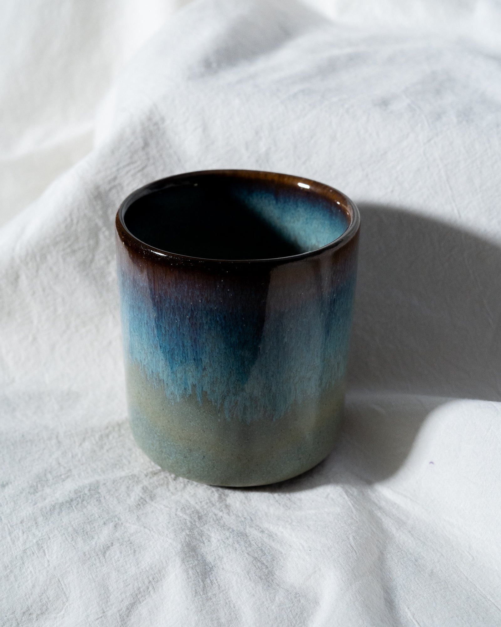 Eine Keramiktasse mit blau-braunem Farbverlauf steht auf einem weißen Tuch.