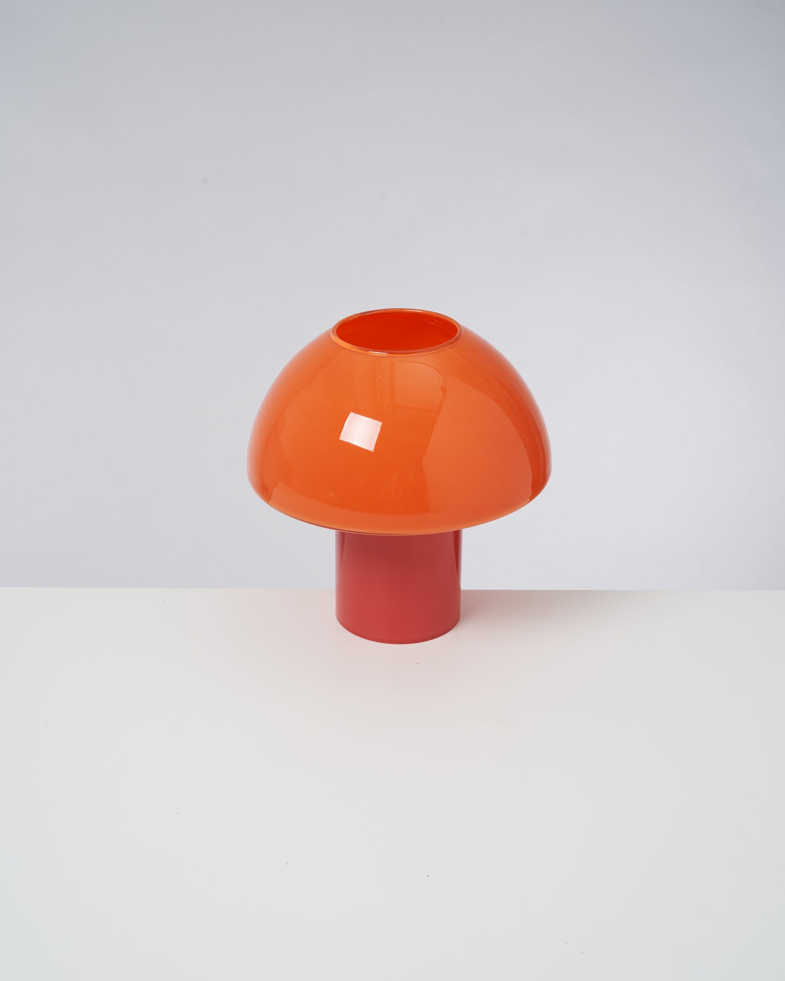 Orangefarbene Lampe in Pilzform auf einem Tisch vor grauem Hintergrund.
