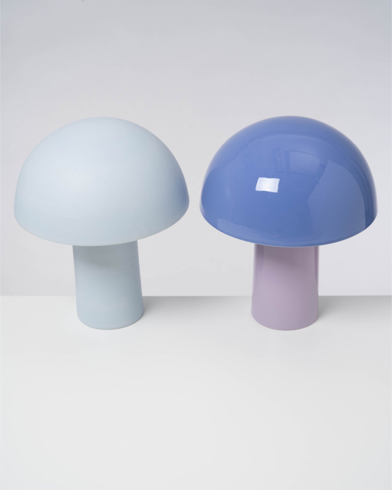 Zwei pilzförmige Lampen in Hellblau und Blau mit glatten, glänzenden Oberflächen auf weißem Hintergrund.
