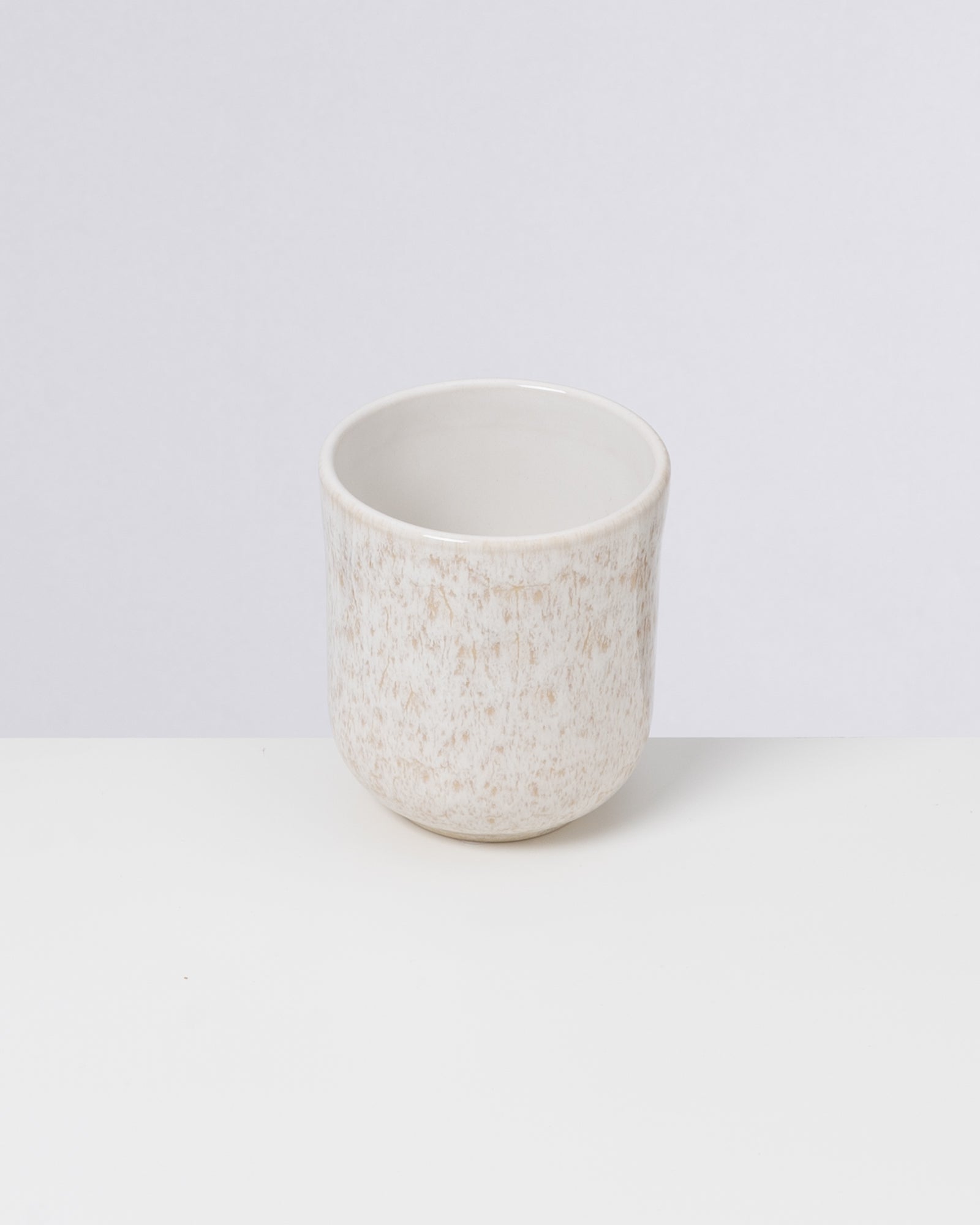 Beiger Keramikbecher mit dezenter Musterung auf weißem Hintergrund.