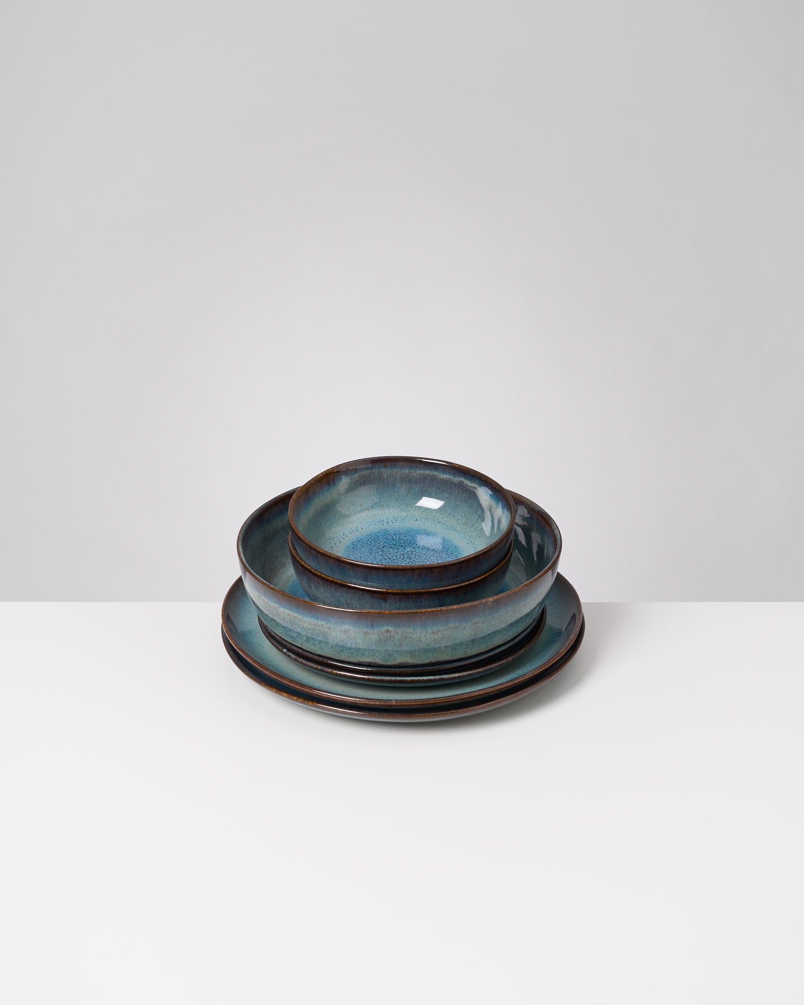Ein gestapeltes Set aus blauen, handgefertigten Keramikschalen und Tellern auf einem weißen Hintergrund.