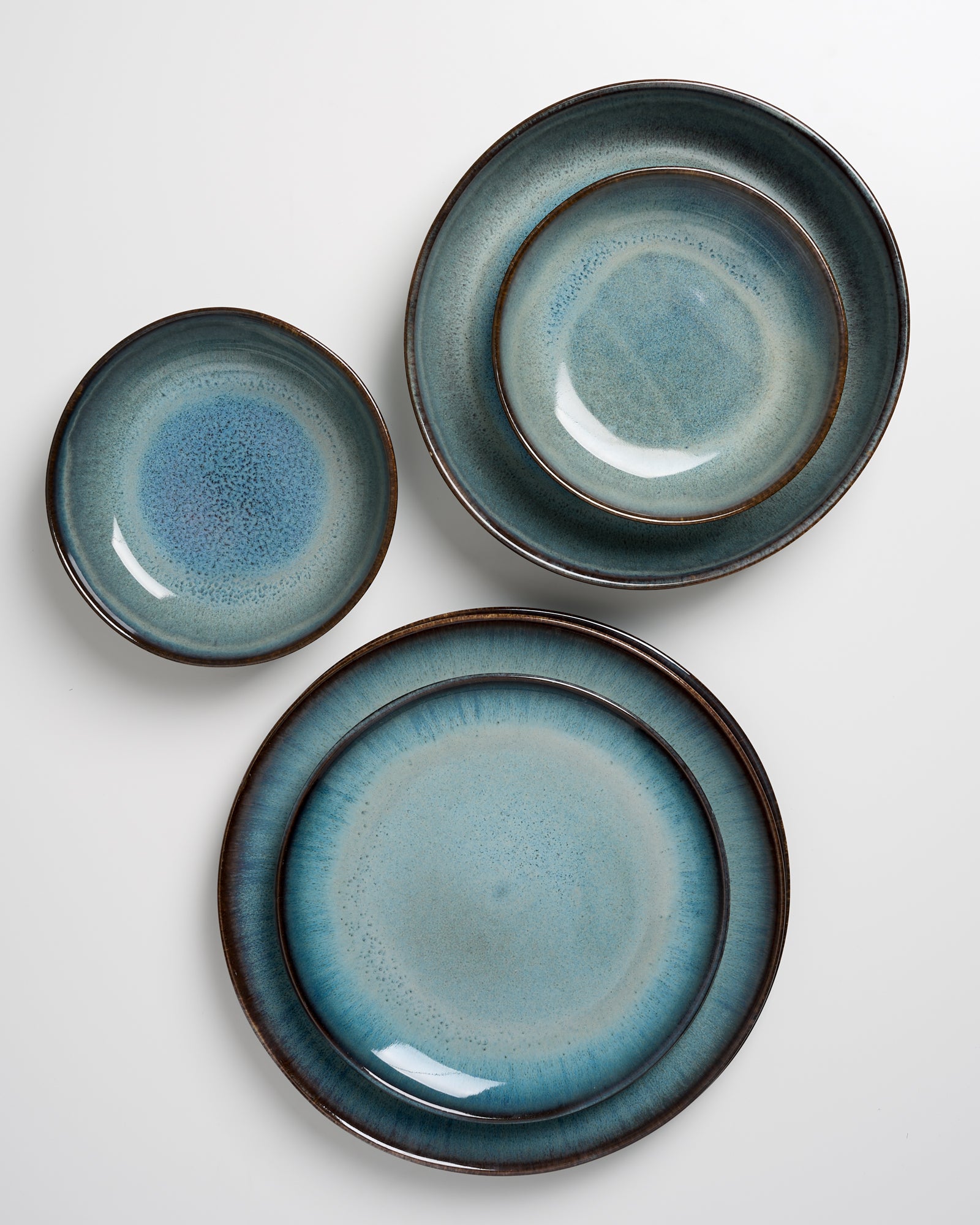 Drei blaue Keramikteller in unterschiedlichen Größen auf einer weißen Oberfläche angeordnet.