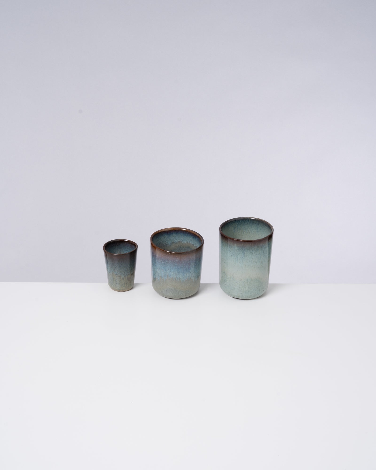 Drei unterschiedlich große Keramiktassen in Blau- und Brauntönen stehen auf einer weißen Oberfläche.