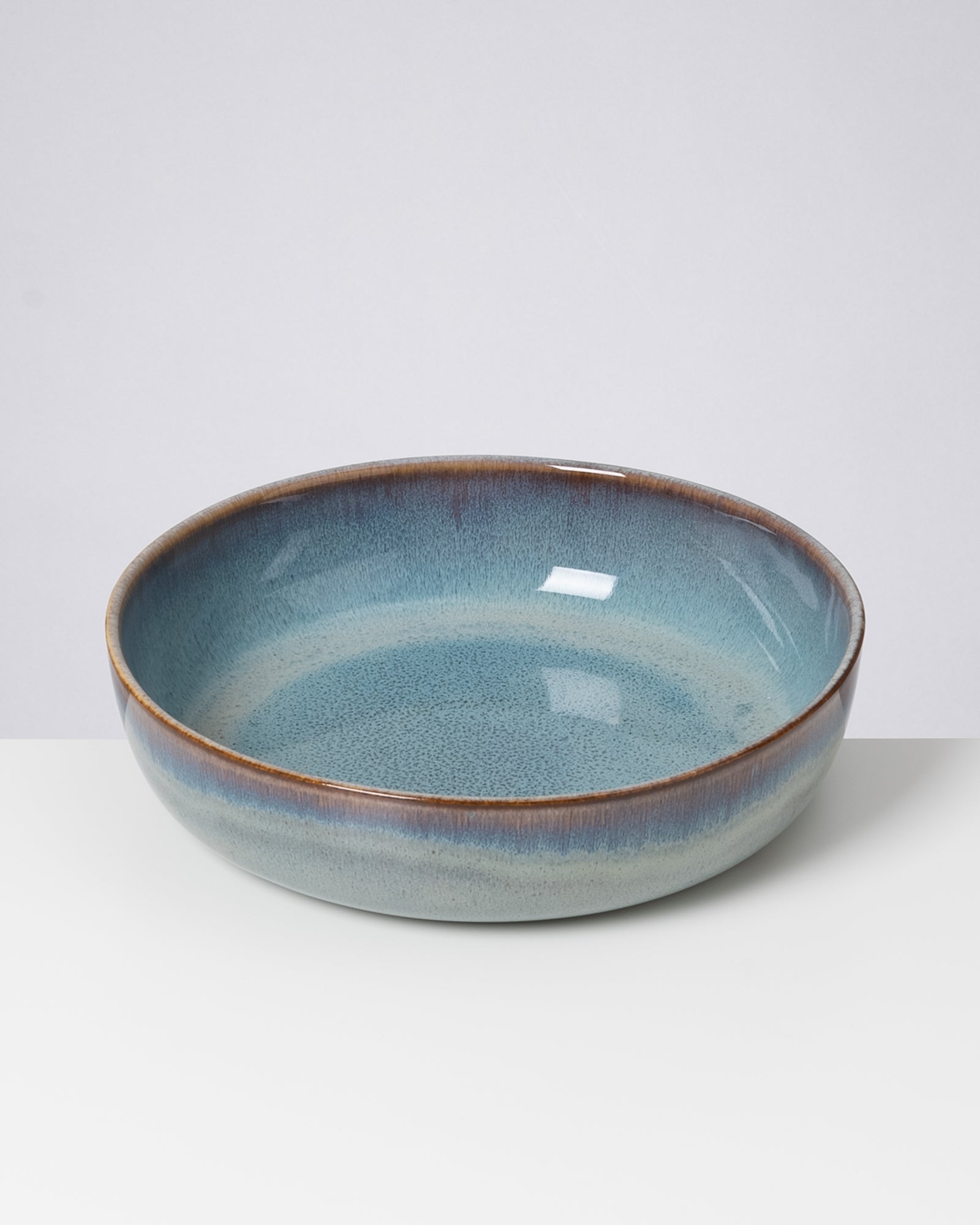 Eine runde, blau-grün glasierte Keramikschale auf einem weißen Untergrund.