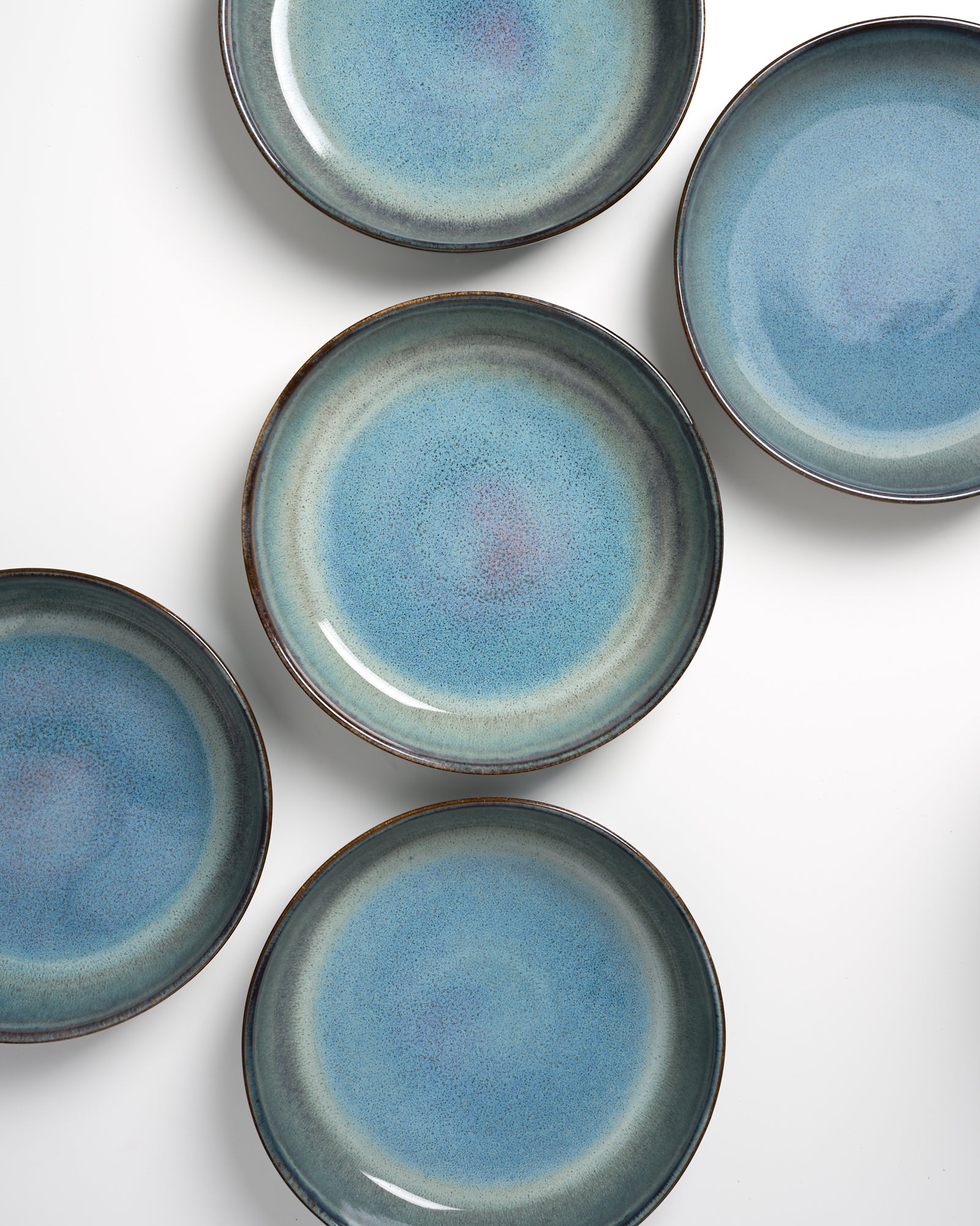 Fünf blaue, runde Teller mit dunklen Rändern, gleichmäßig auf einem weißen Hintergrund angeordnet.