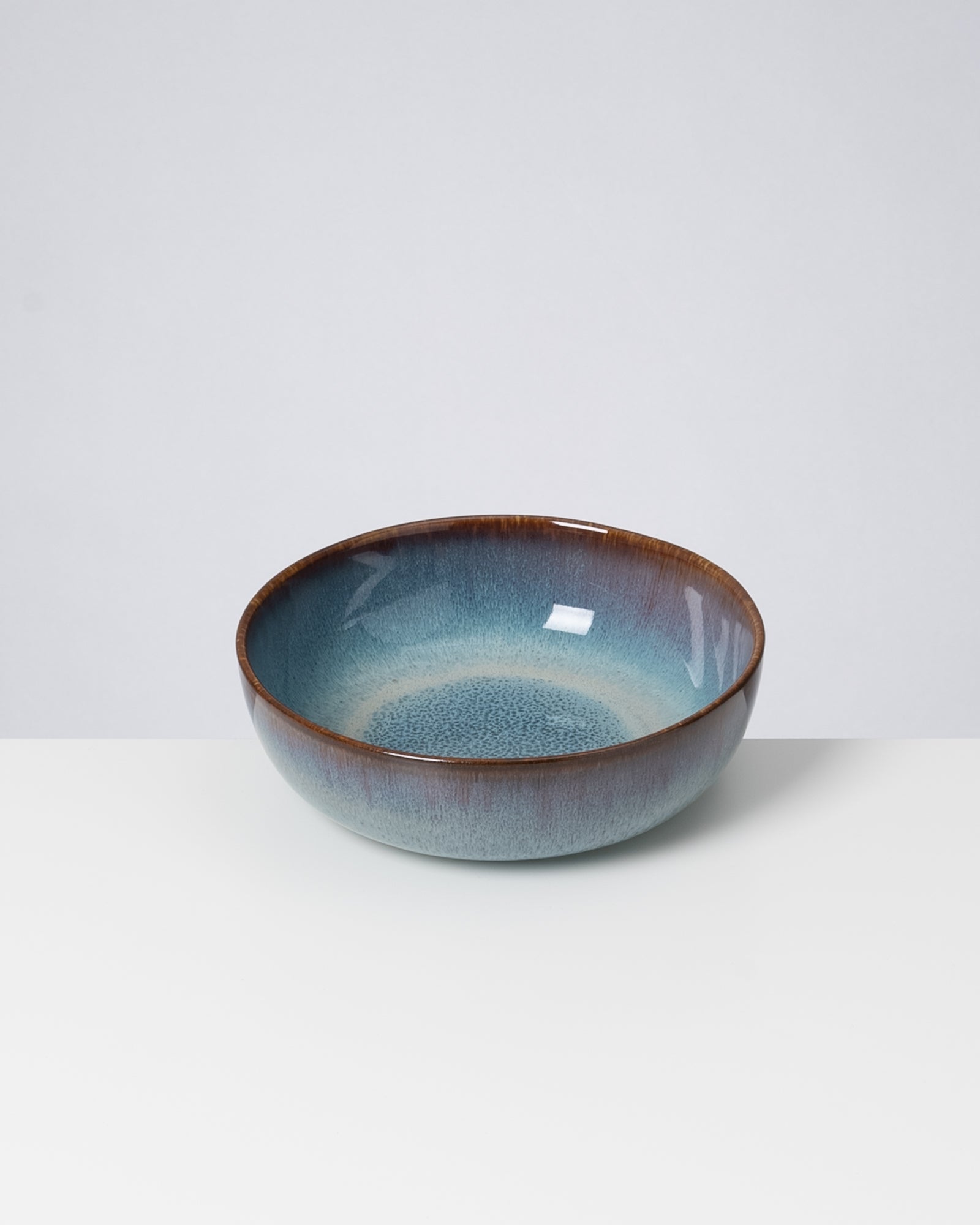 Keramikschale mit blau-brauner Glasur auf weißem Untergrund.