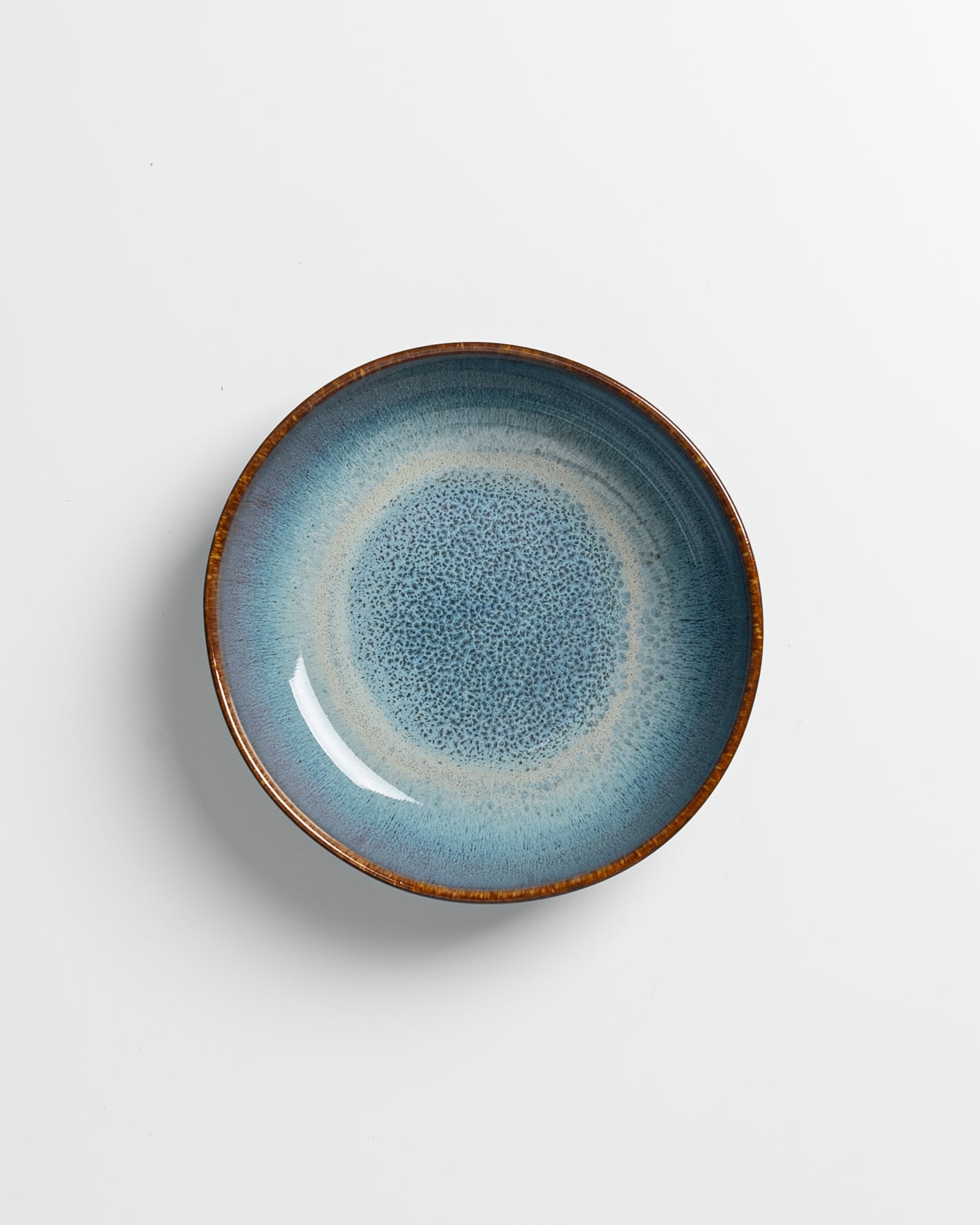 Blauer Keramikteller mit braunem Rand, zentralen Farbübergängen und gesprenkeltem Muster auf weißem Hintergrund.