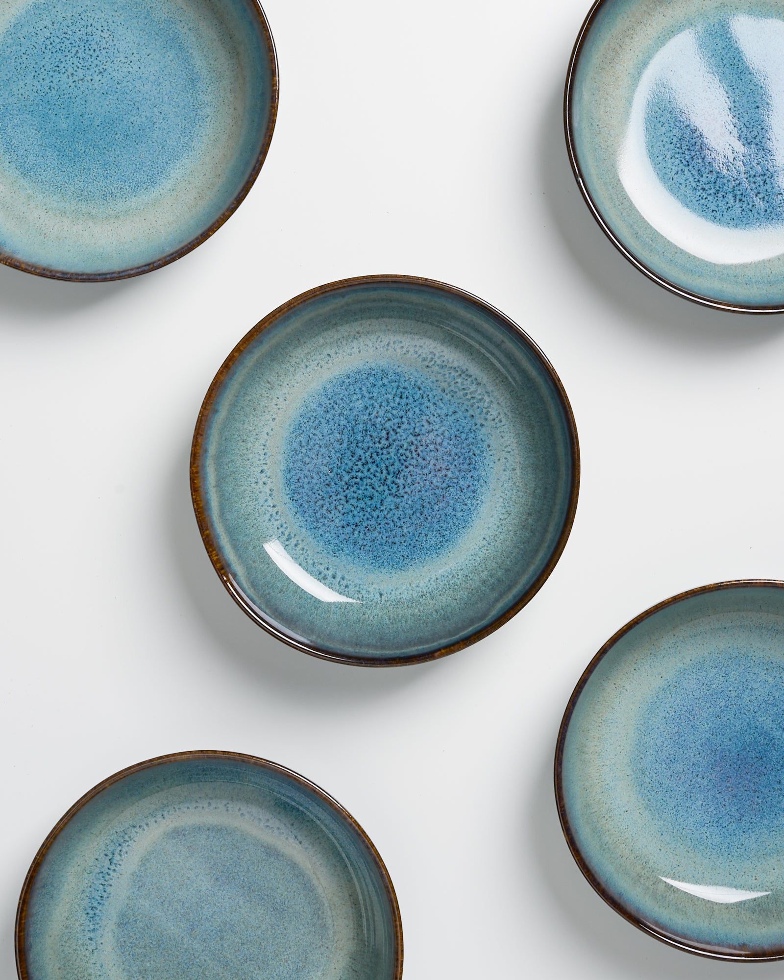 Fünf blaue, keramische Teller mit natürlichen Farbverläufen auf weißem Hintergrund angeordnet.