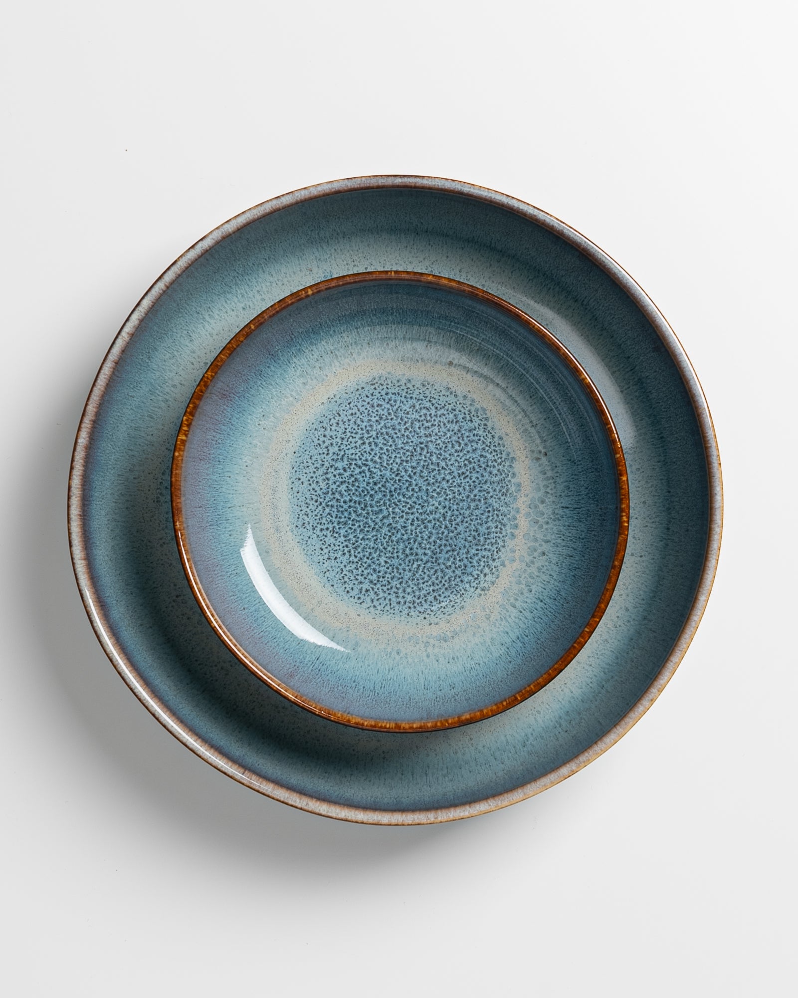 Zwei übereinanderliegende, blau-graue Keramikteller mit braunen Rändern auf einem weißen Hintergrund.